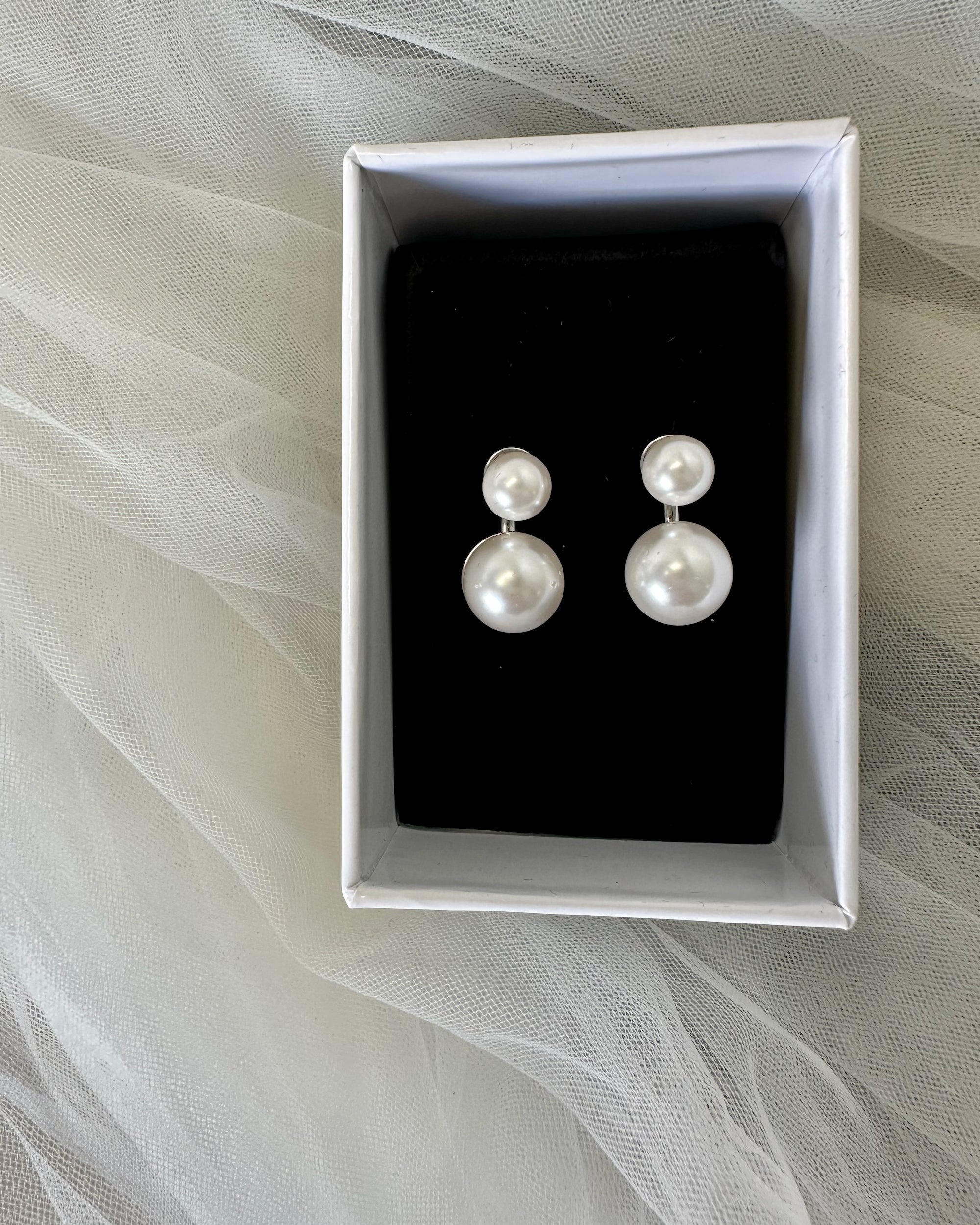 Pair of pearl earrings in a box on a sheer fabric background