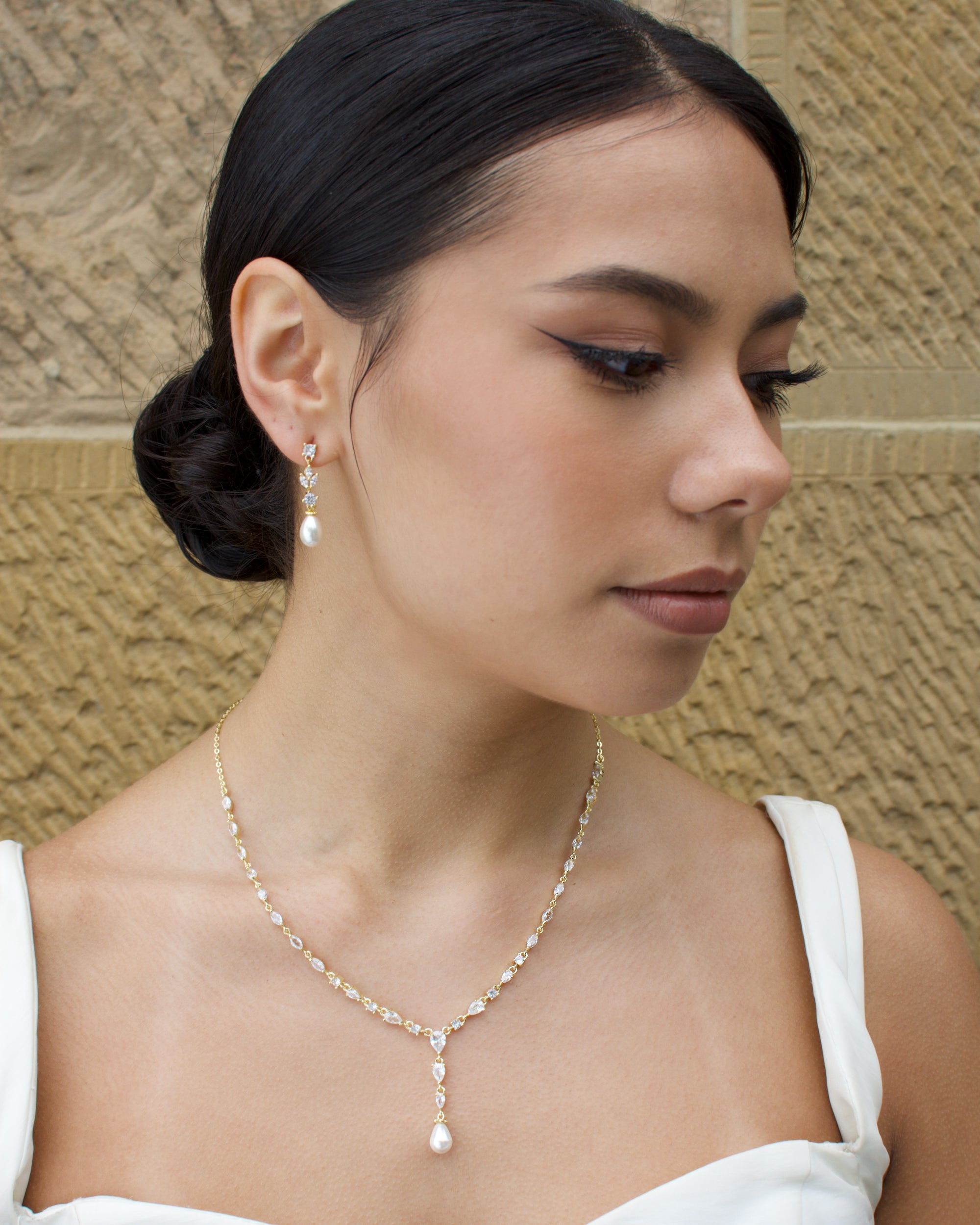Woman wearing a pearl necklace and earrings against a textured wall.