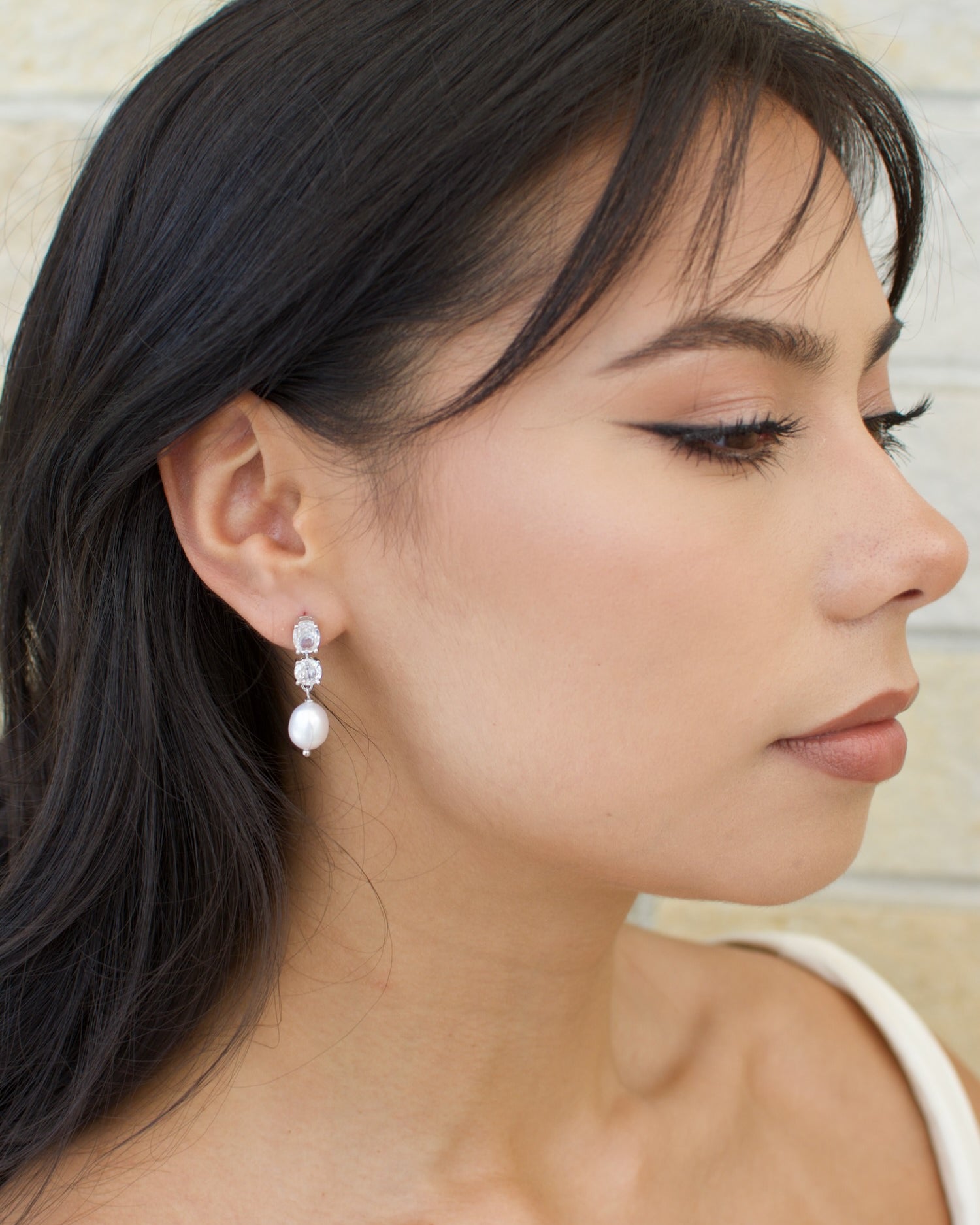 A close-up image of a woman's face wearing a white gold finish and pearl earrings.