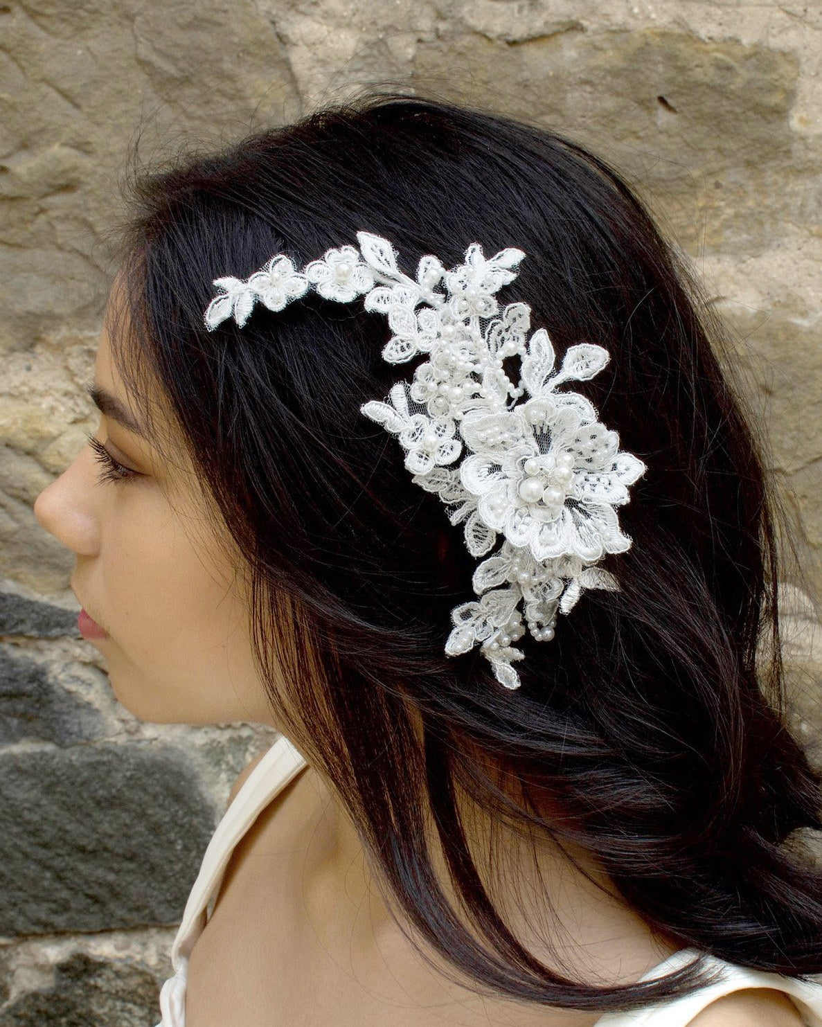 White lace bridal side comb with pearls worn by a bride in front of a stone wall
