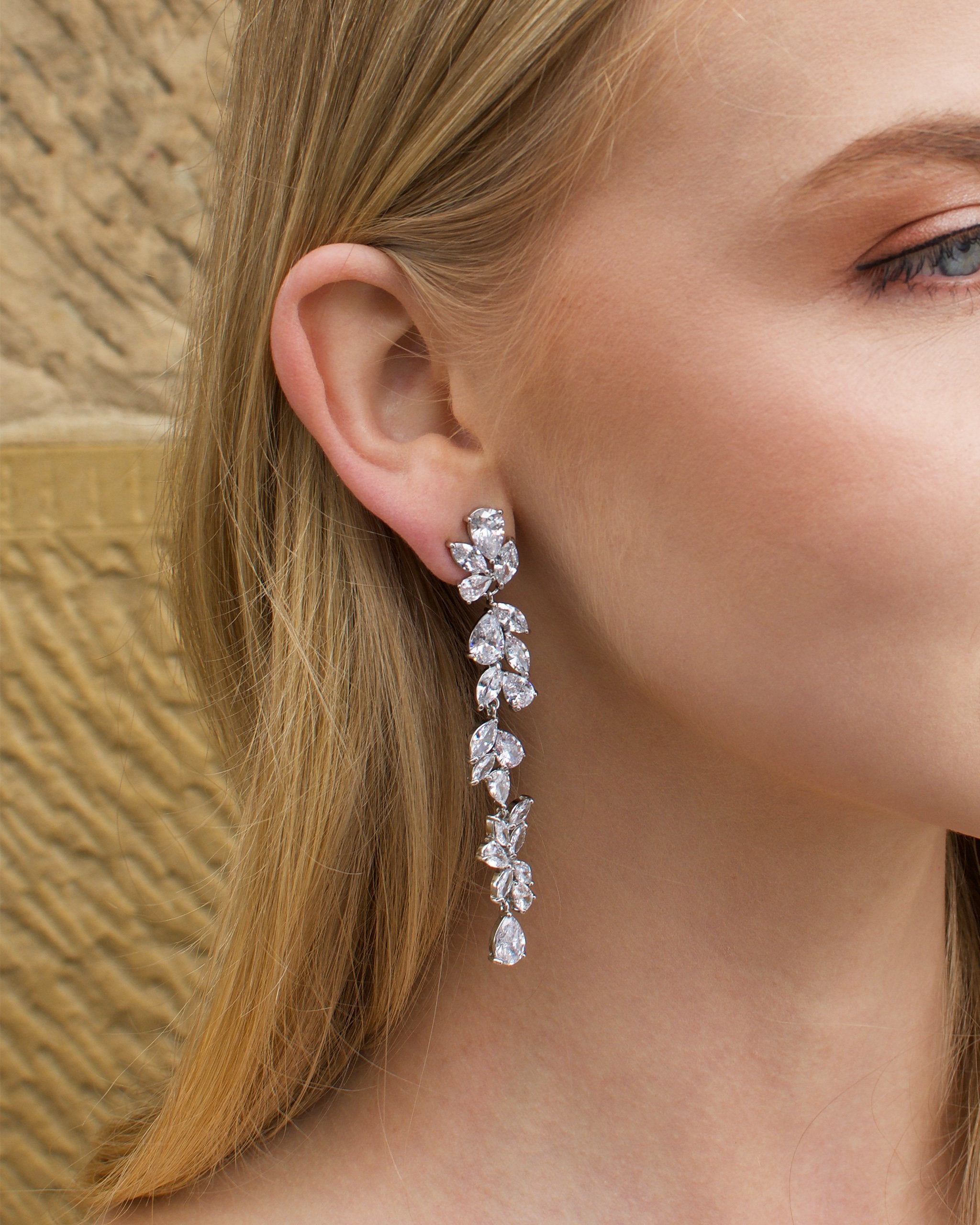 Long thin silver earring with stones worn by a blonde model with a sandstone wall backdrop