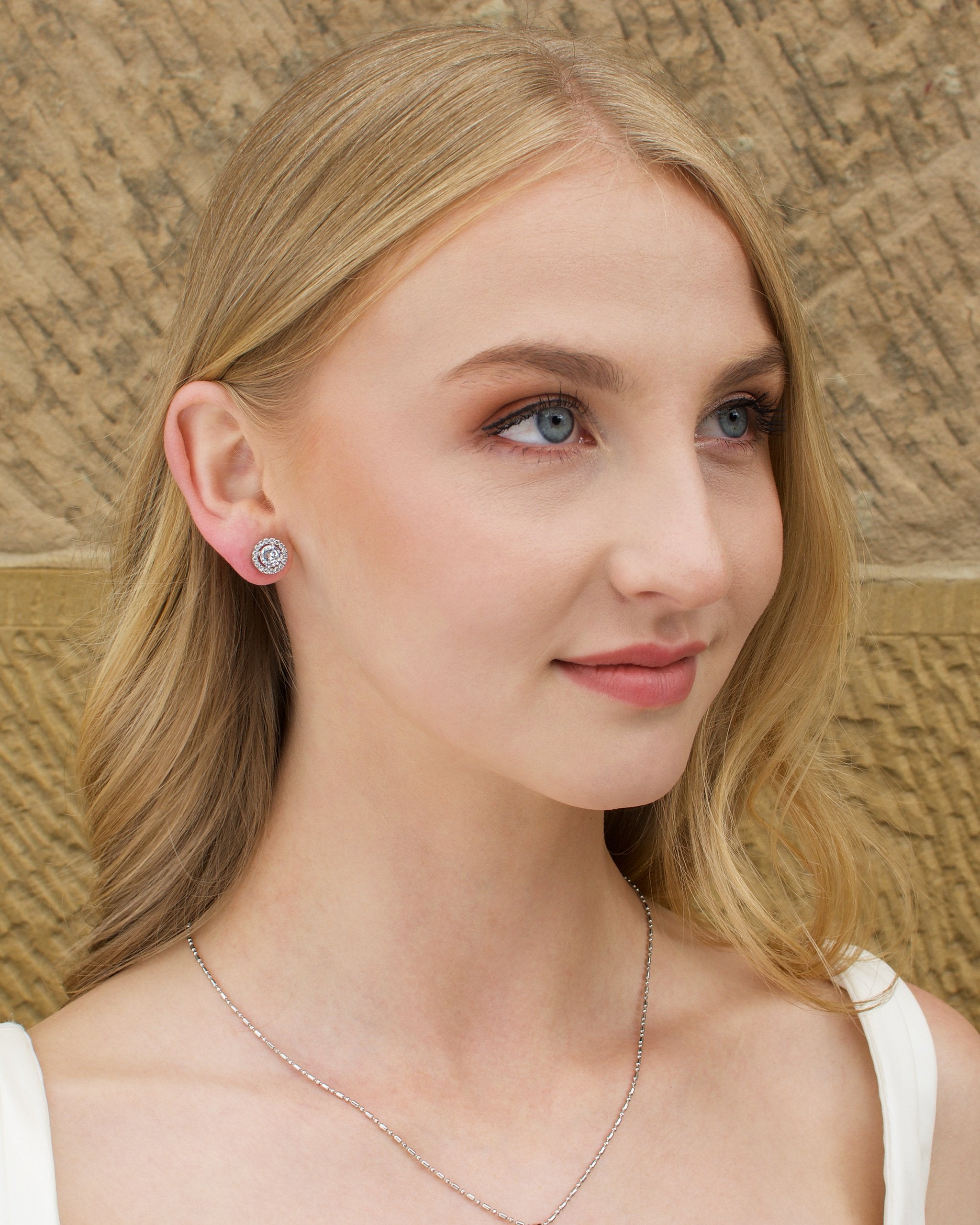 Model wears a silver chain pendant necklace with a single stone and a matching stud earring