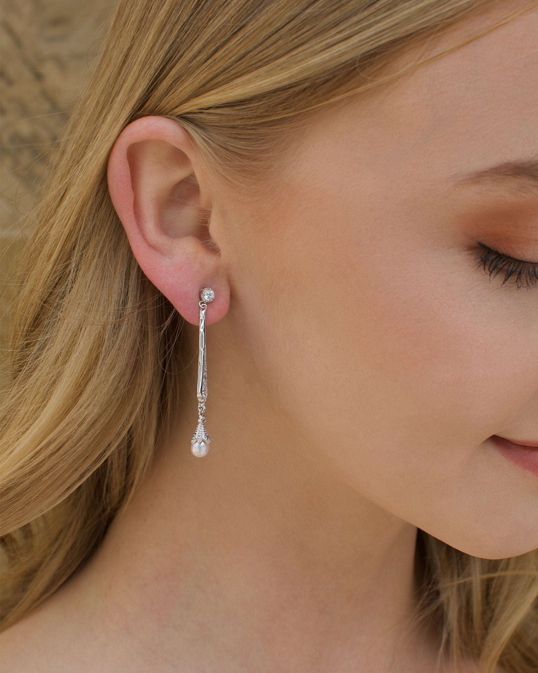 A long silver bridal earring with a hanging pearl worn by a blonde model