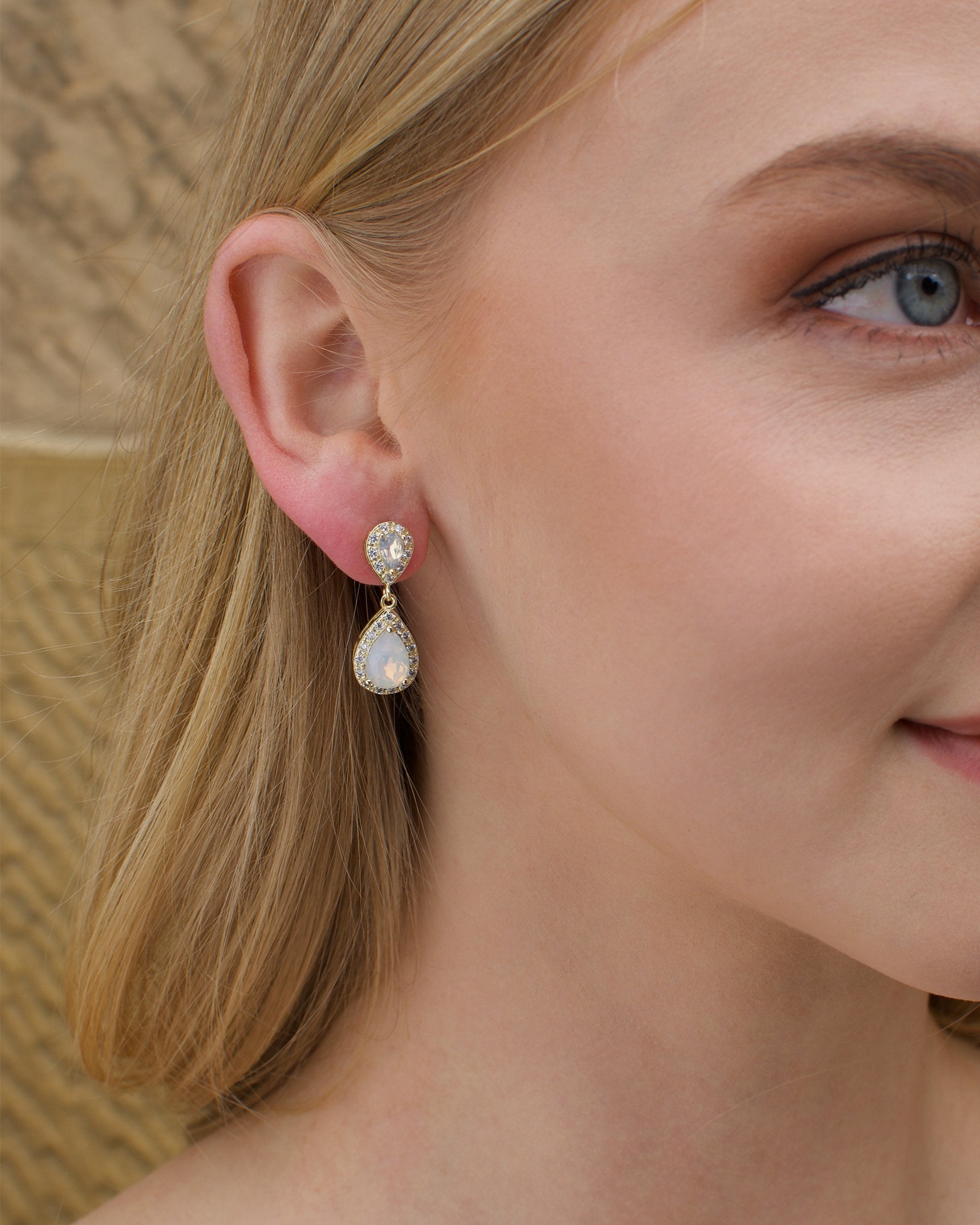 A blonde model wears a gold and white opal earring with a stone wall background