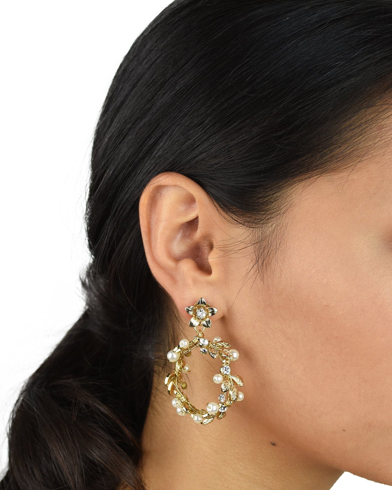 Model wears a gold hoop shape earring. She has dark hair.