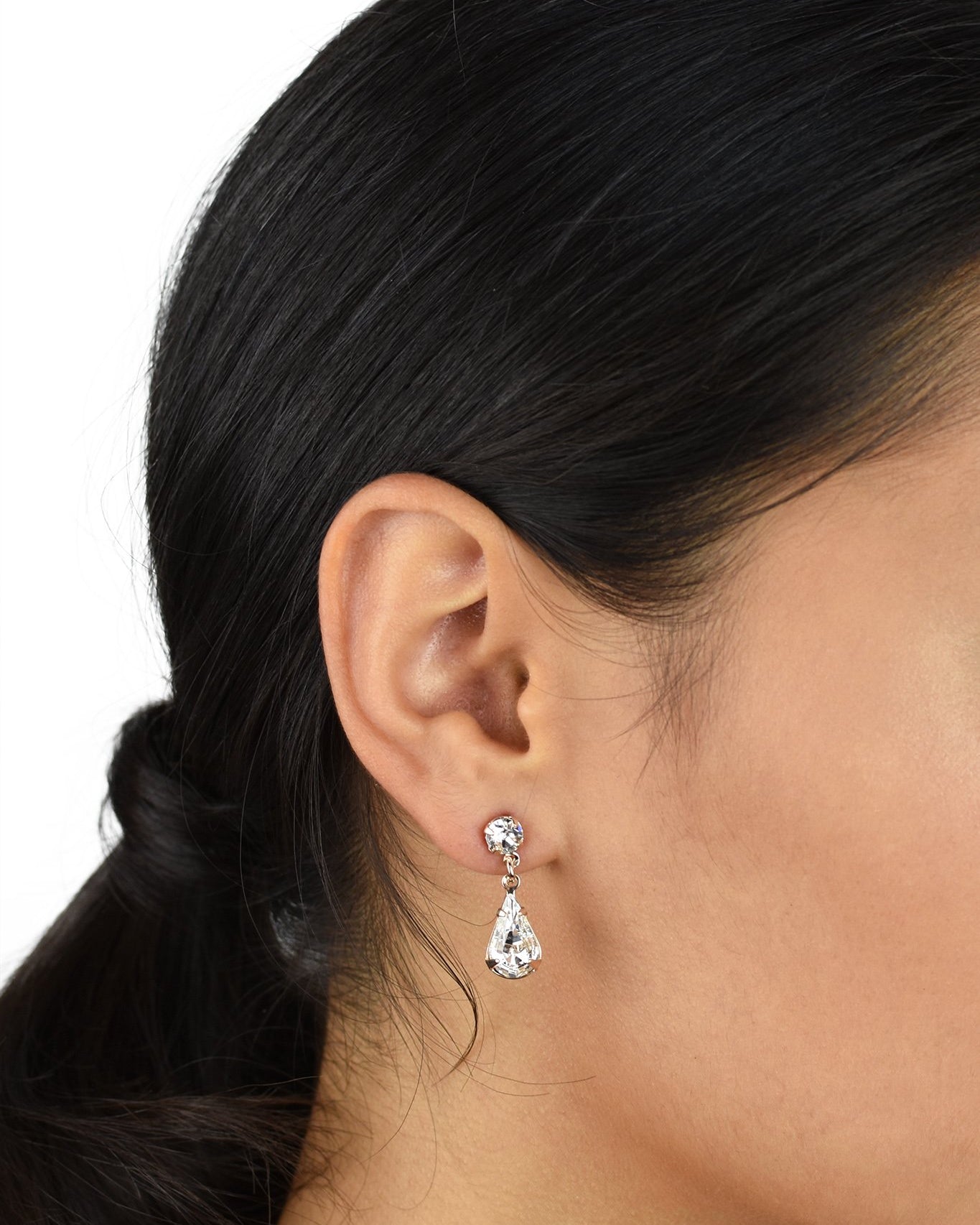 A model with black hair wears a rose gold teardrop earring in her ear against a white background