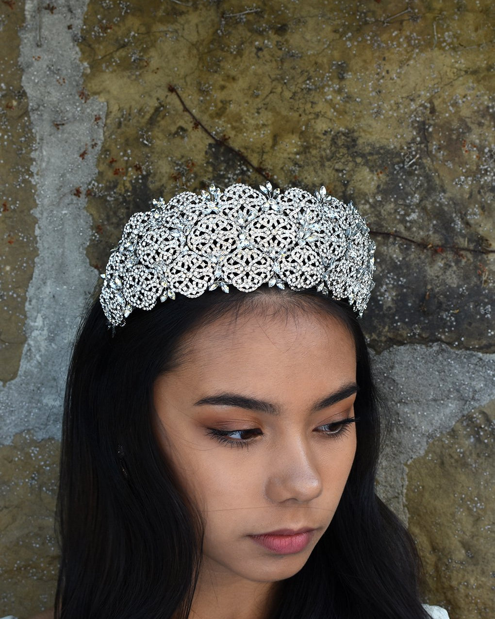 Very high Bridal Tiara with hundreds of tiny crystals worn by a dark hair bride with a stone wall backdrop