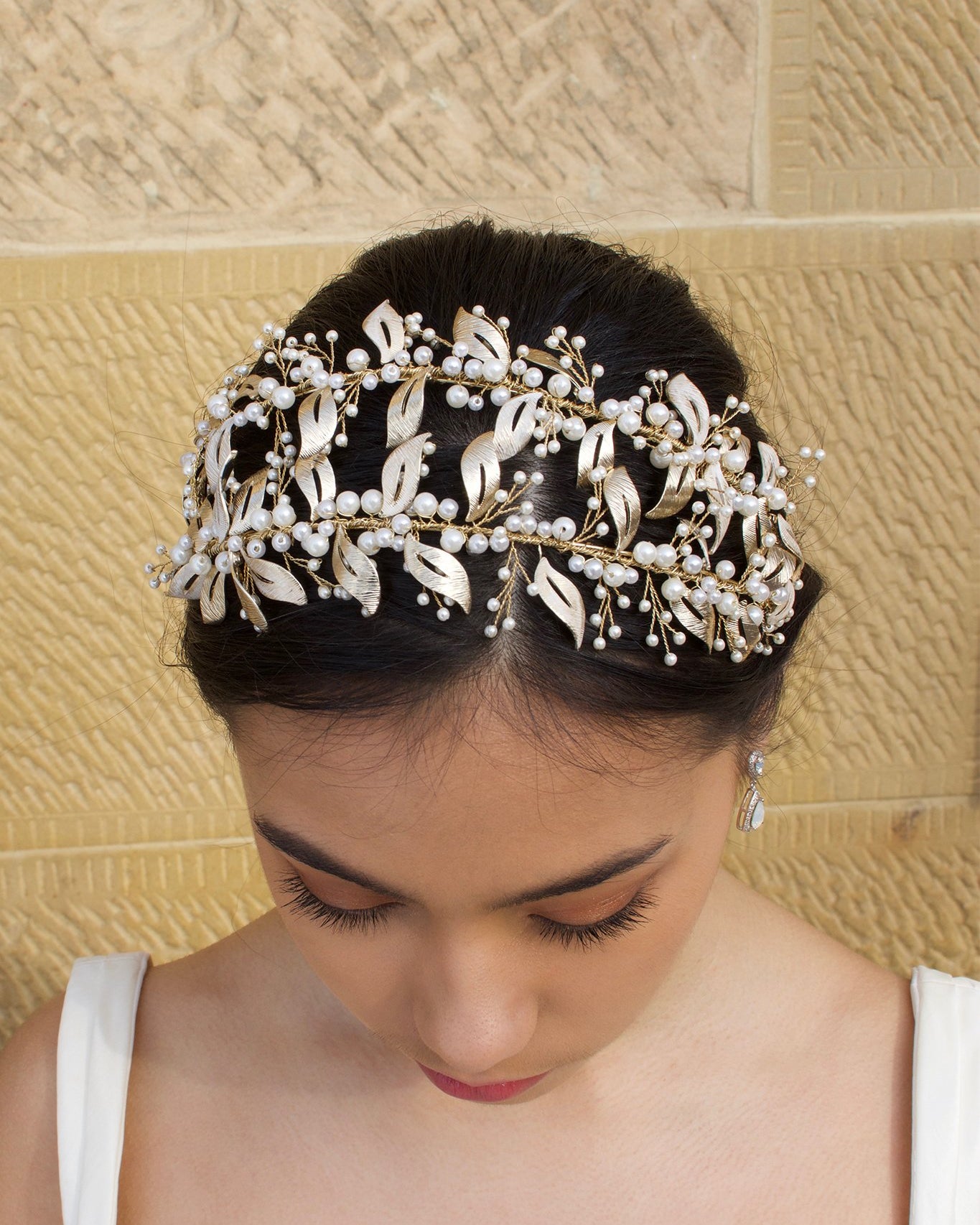 Double row pale gold headband with pearls worn by a dark hair model with a sandstone wall