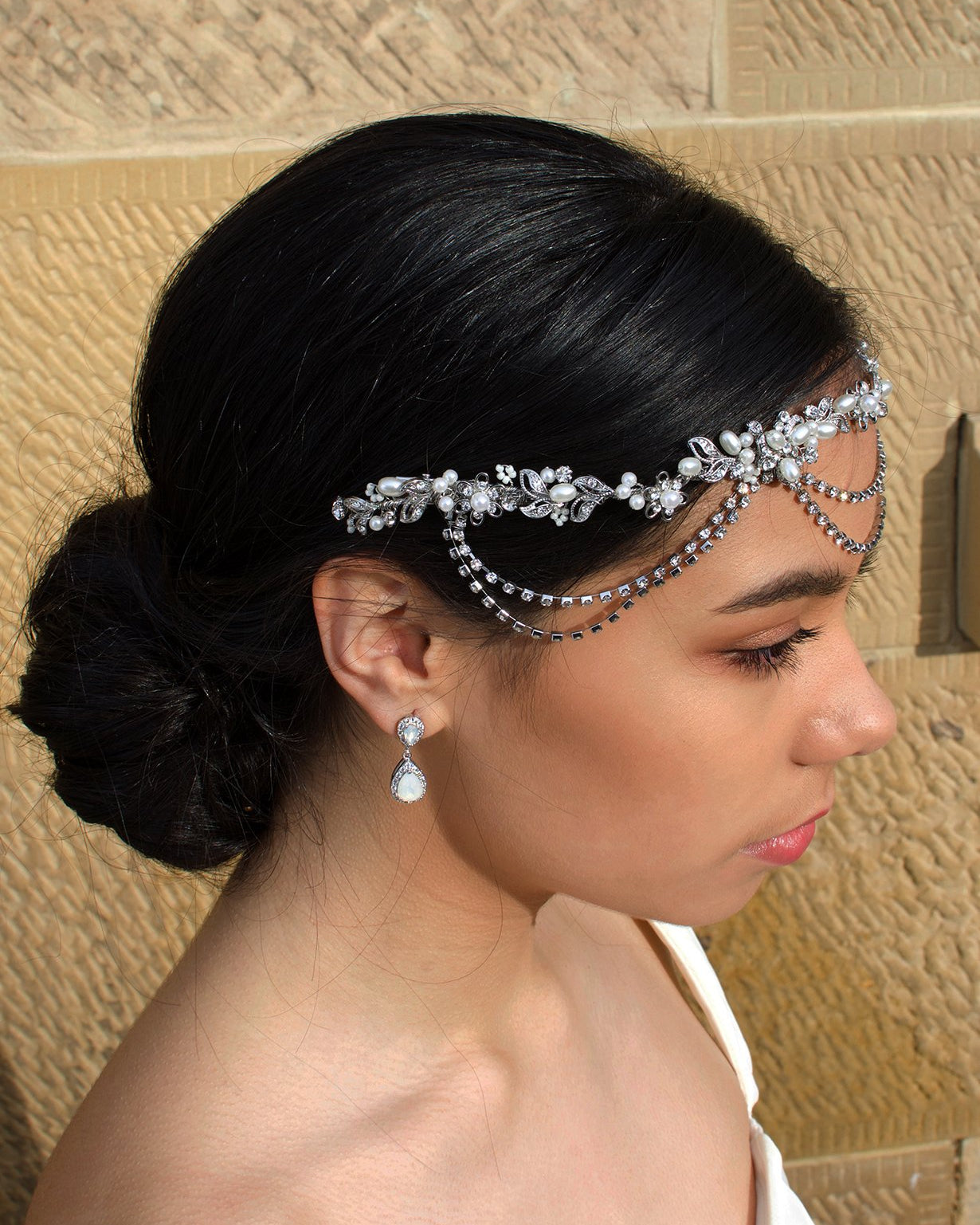 A side view of a bridal vine worn across the forehead of a dark hair bride. With a stone wall behind