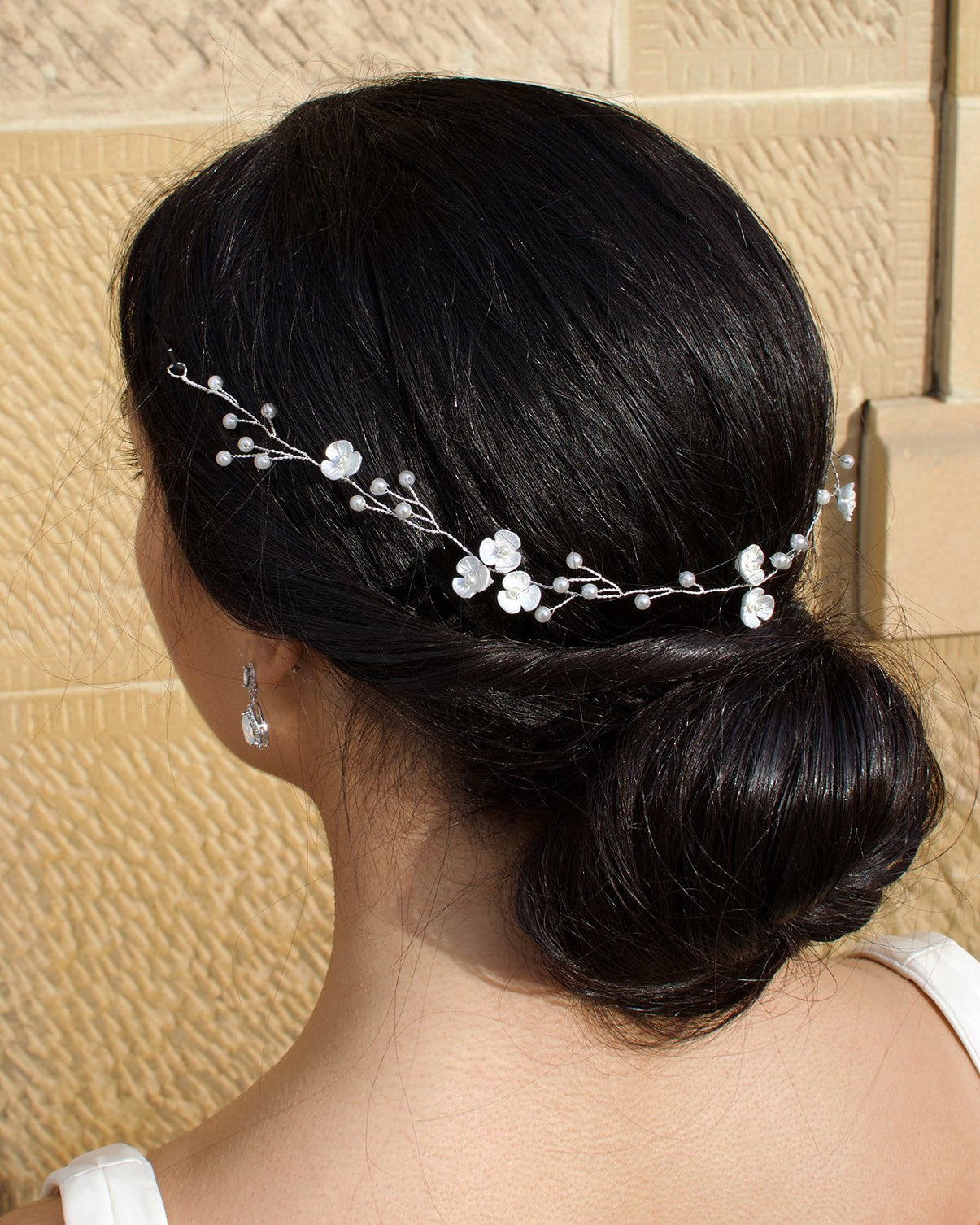 Thin wire bridal vine with pearls and small flowers on a black hair bride pictured in front of a stone wall