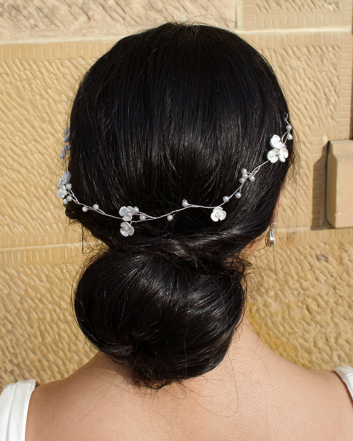 Single Strand Silver wire pearl vine worn at the back of a brides head shown with a stone wall behind