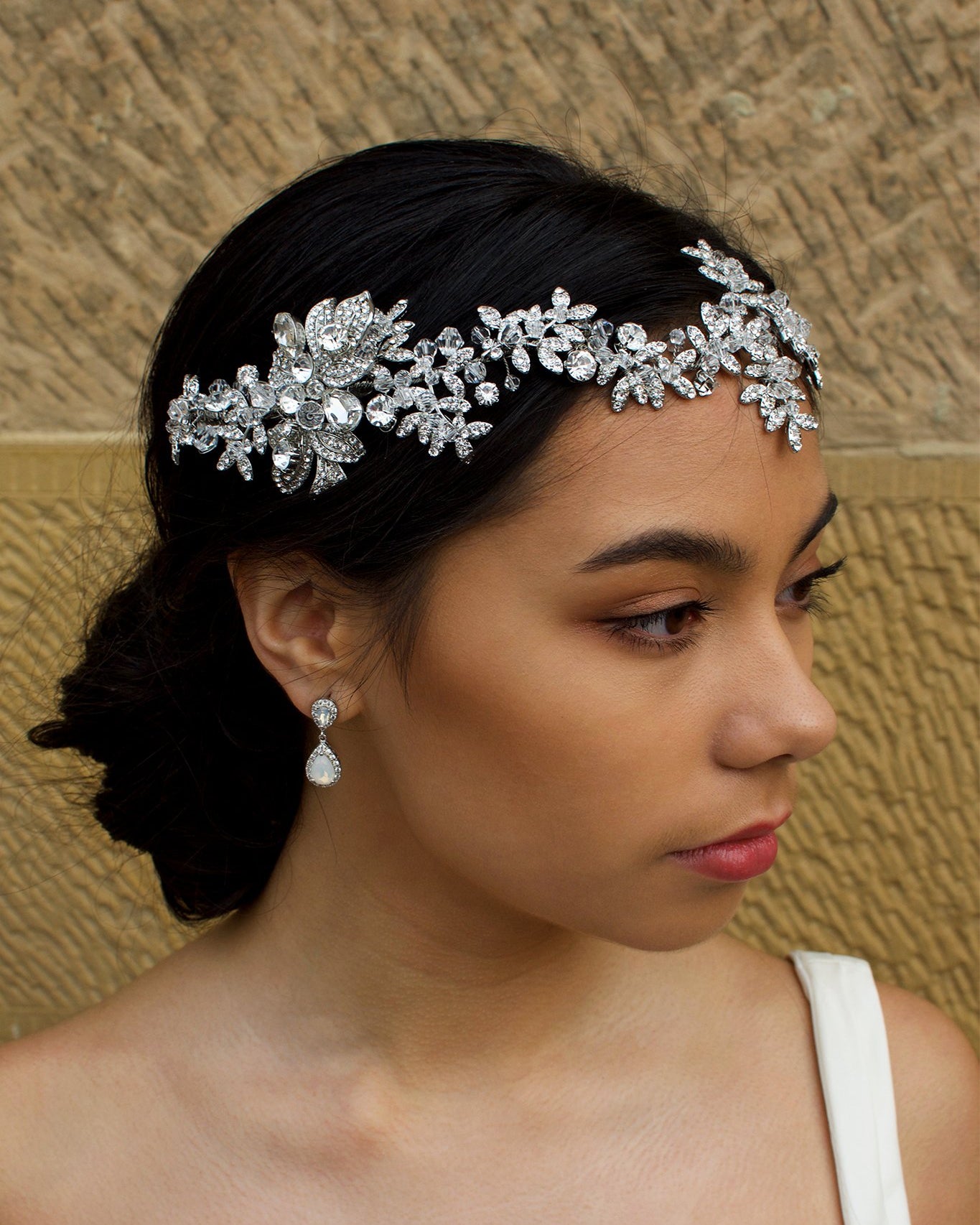 Dark Silver vine of leaves encrusted with tiny crystals worn across the forehead of a dark haired bride with a stone wall behind