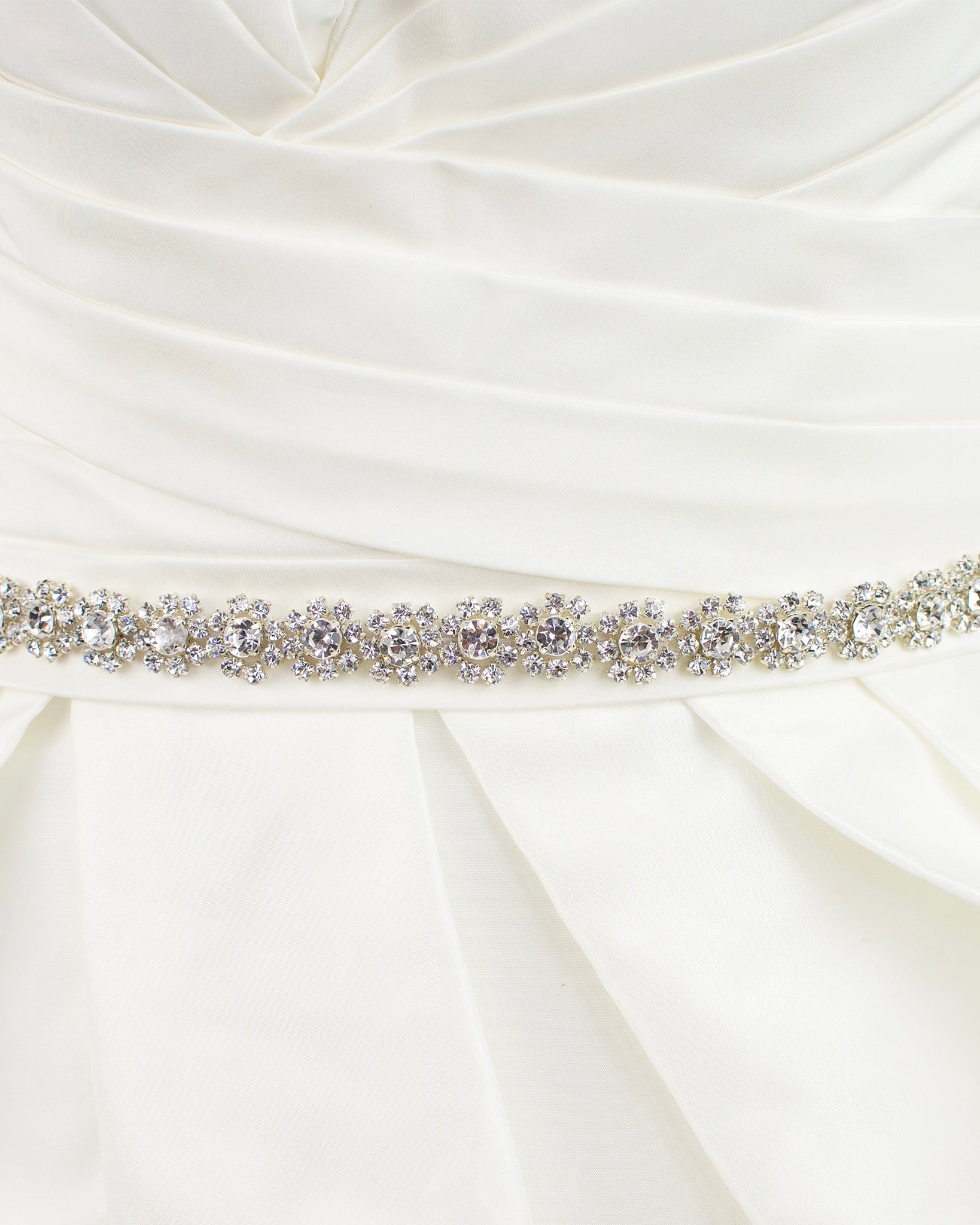 A narrow crystal bridal belt with rings of crystals around the pearls is worn on an ivory bridal gown
