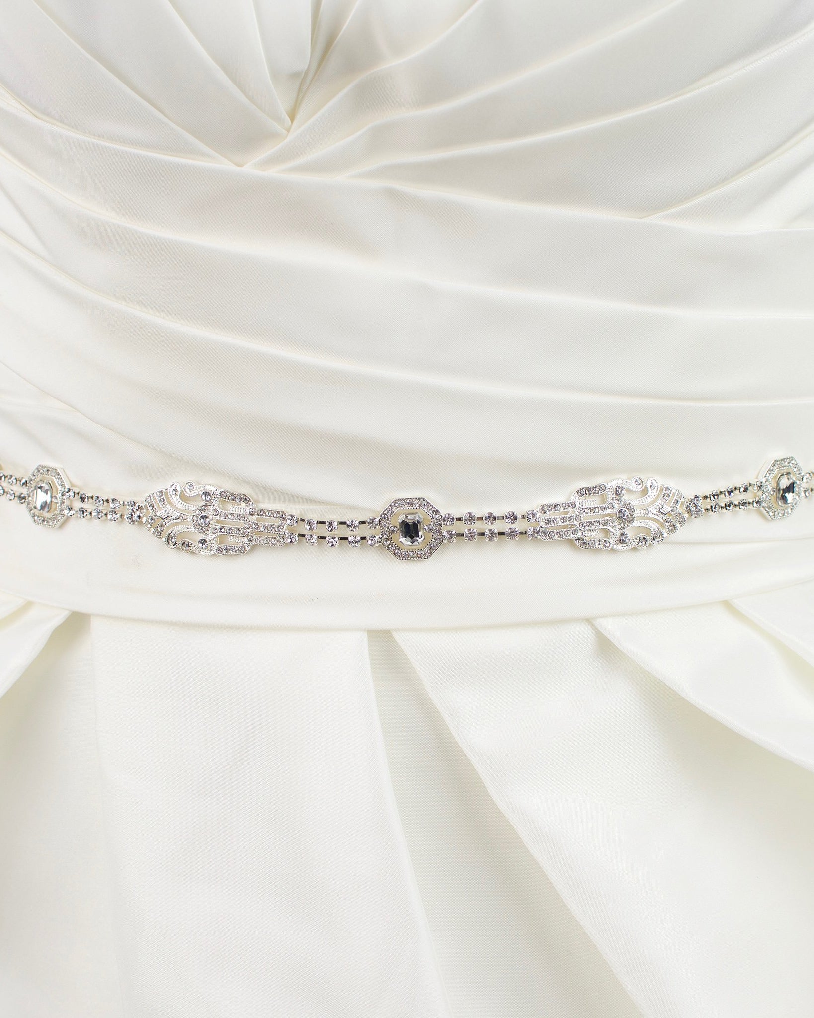A narrow silver chain bridal belt worn on an ivory wedding gown with a white background
