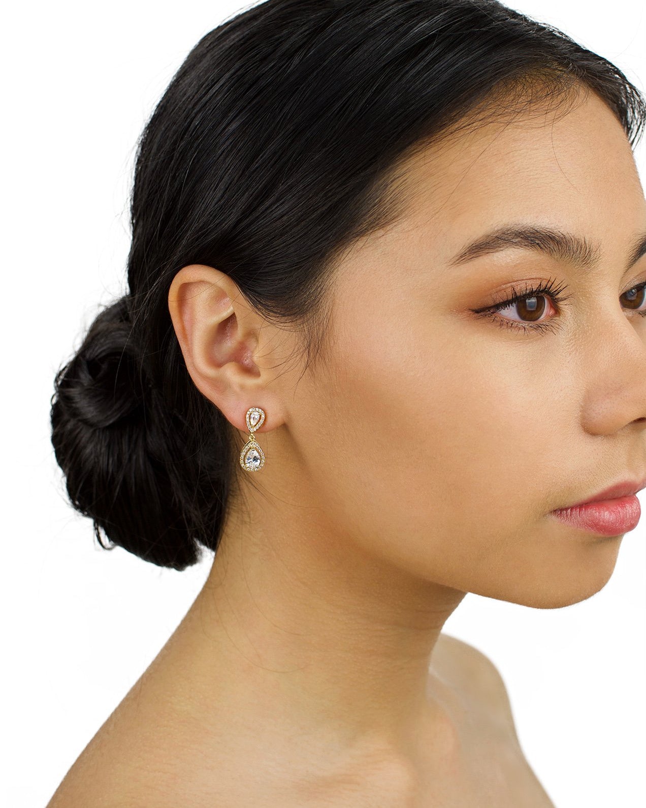 Very small gold drop earring worn by a dark hair bridal model with a white background