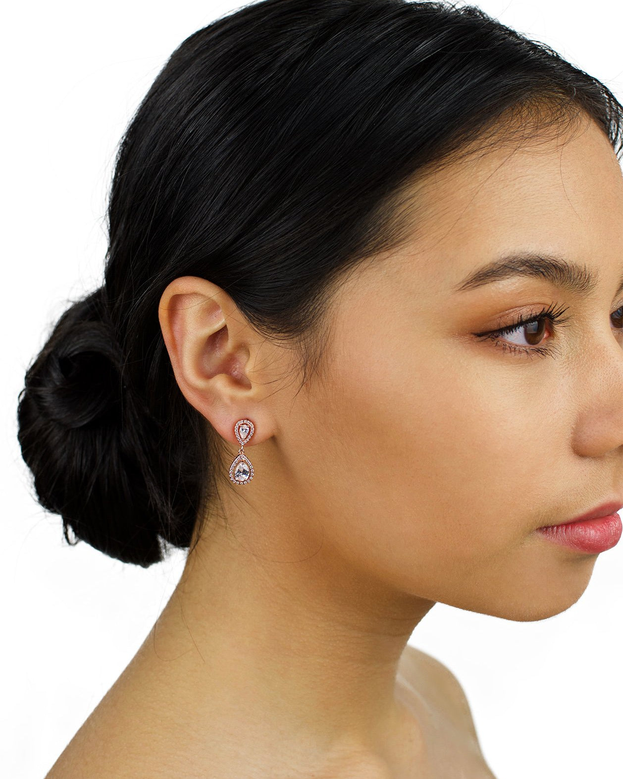 Small pear shape rose gold earring worn by a bridal model with dark hair on a white background