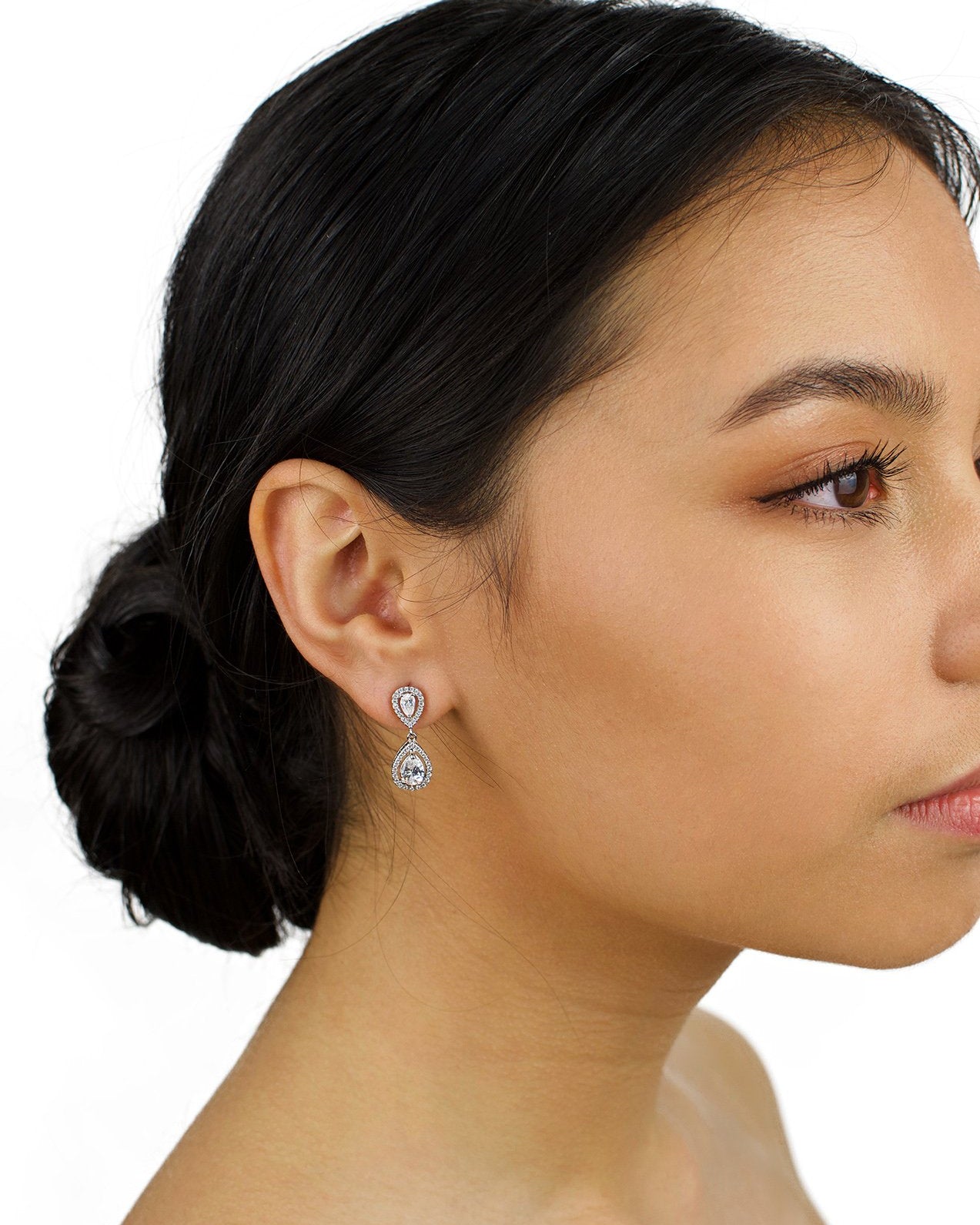 Small silver drop earring worn by a dark hair bride with a white background