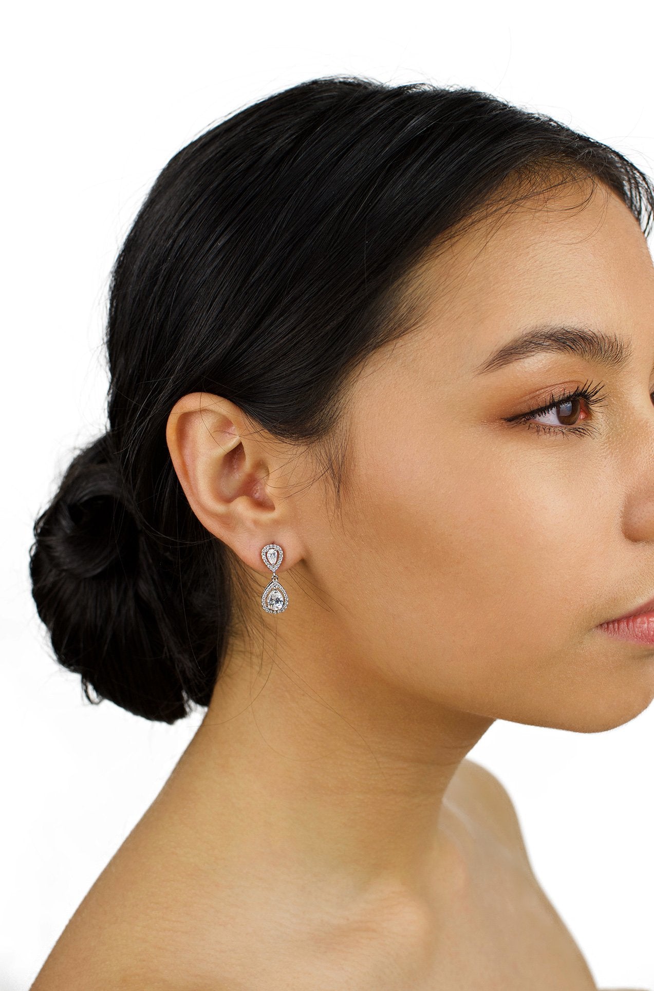 Small silver drop earring worn by a dark hair bride with a white background