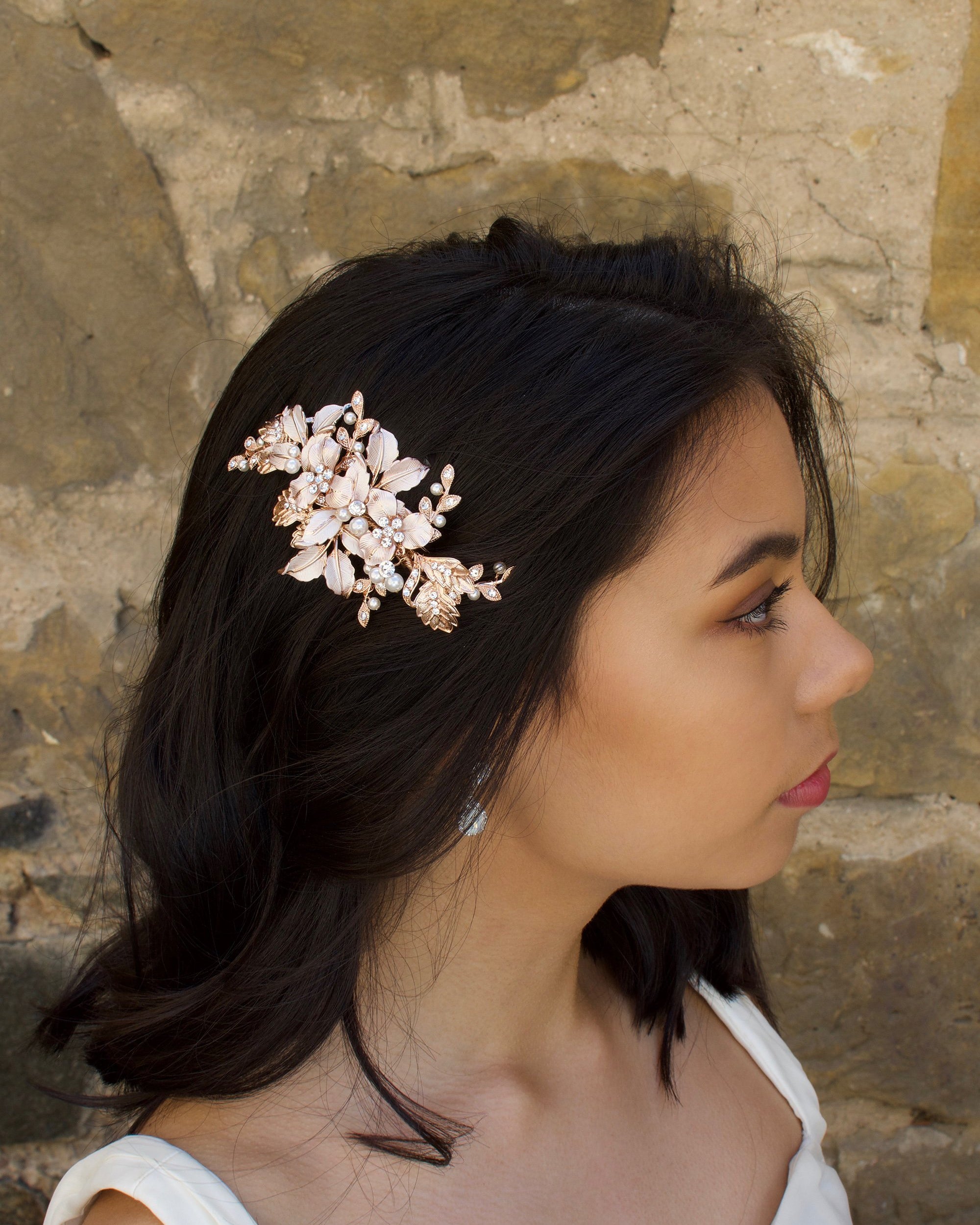 Pale Rose Gold Bridal Comb with leaves and flowers worn by a dark hair bride with a stone wall backdrop