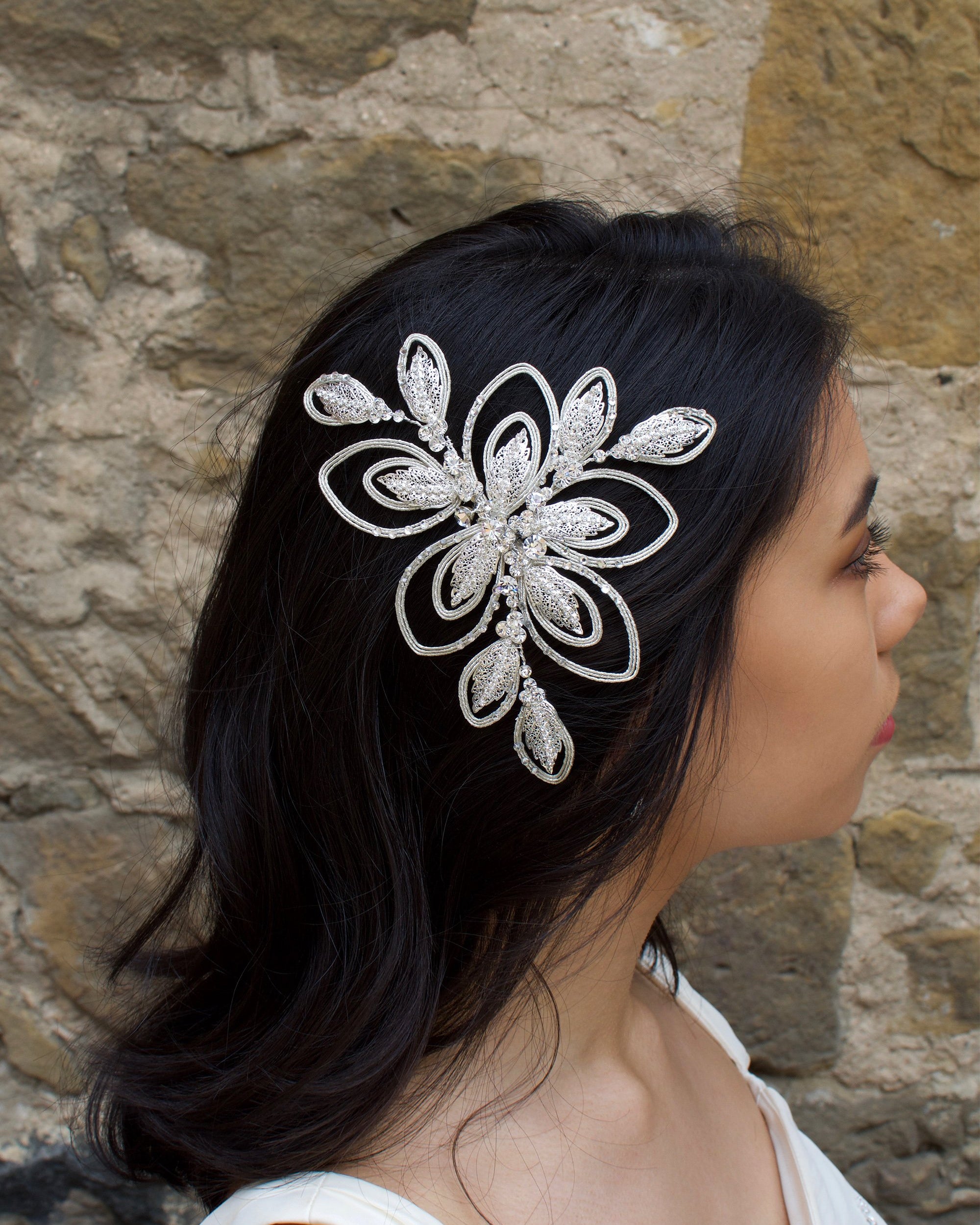 A dark haired bride wears a soft matt silver bridal side comb with a stone wall background