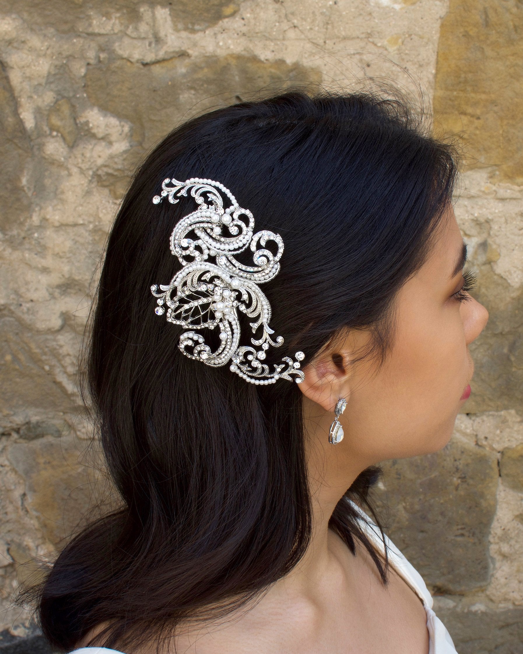 Model Bride wears a swirling side comb in her black hair with a stone wall background