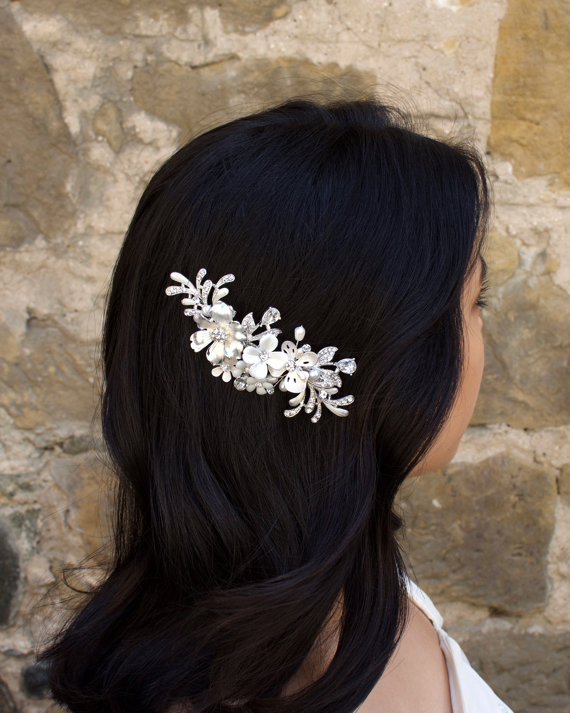 Model with dark hair wears a silver and flower side comb with a stone wall backdrop