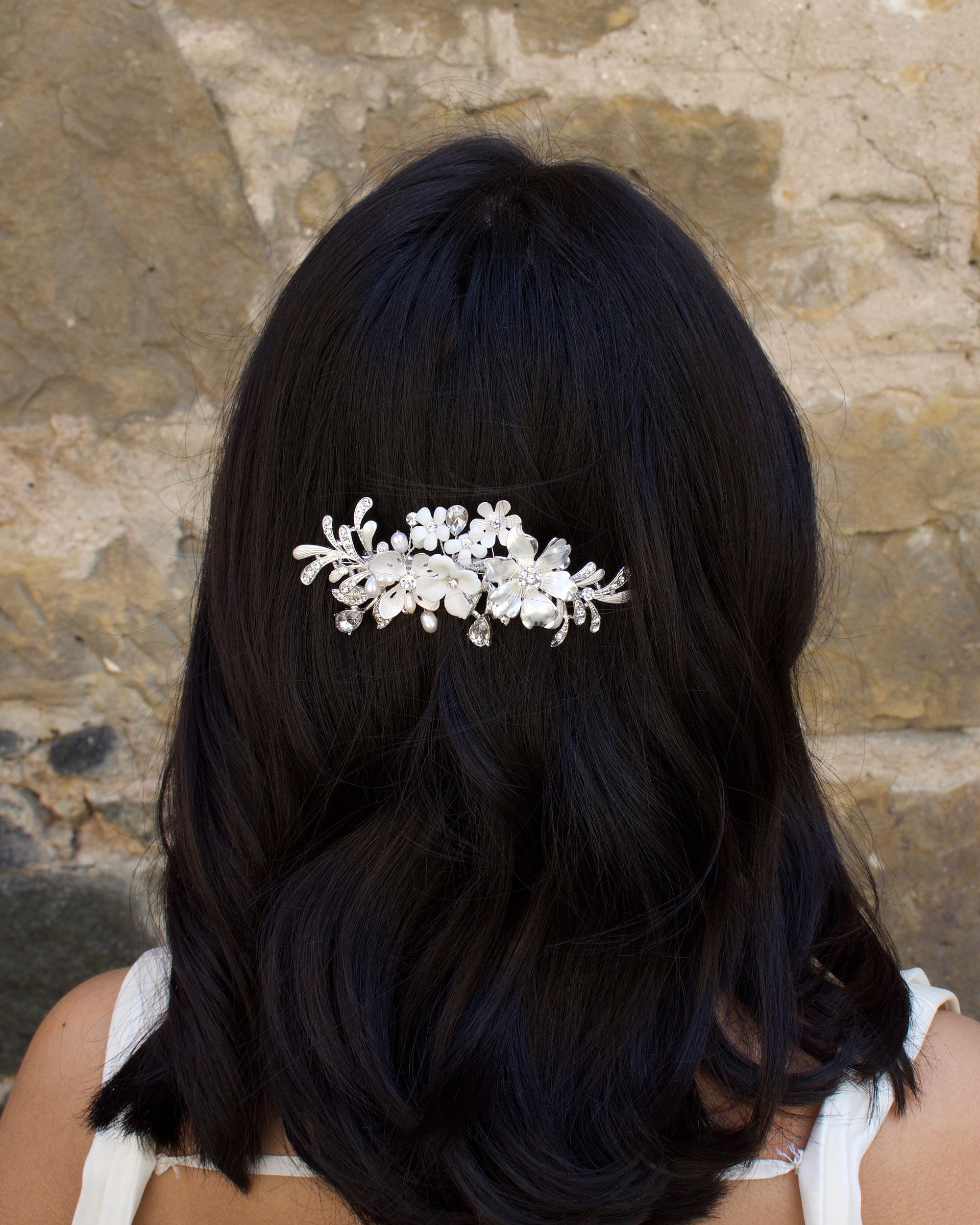 Model with dark hair wears a silver and flower side comb with a stone wall backdrop