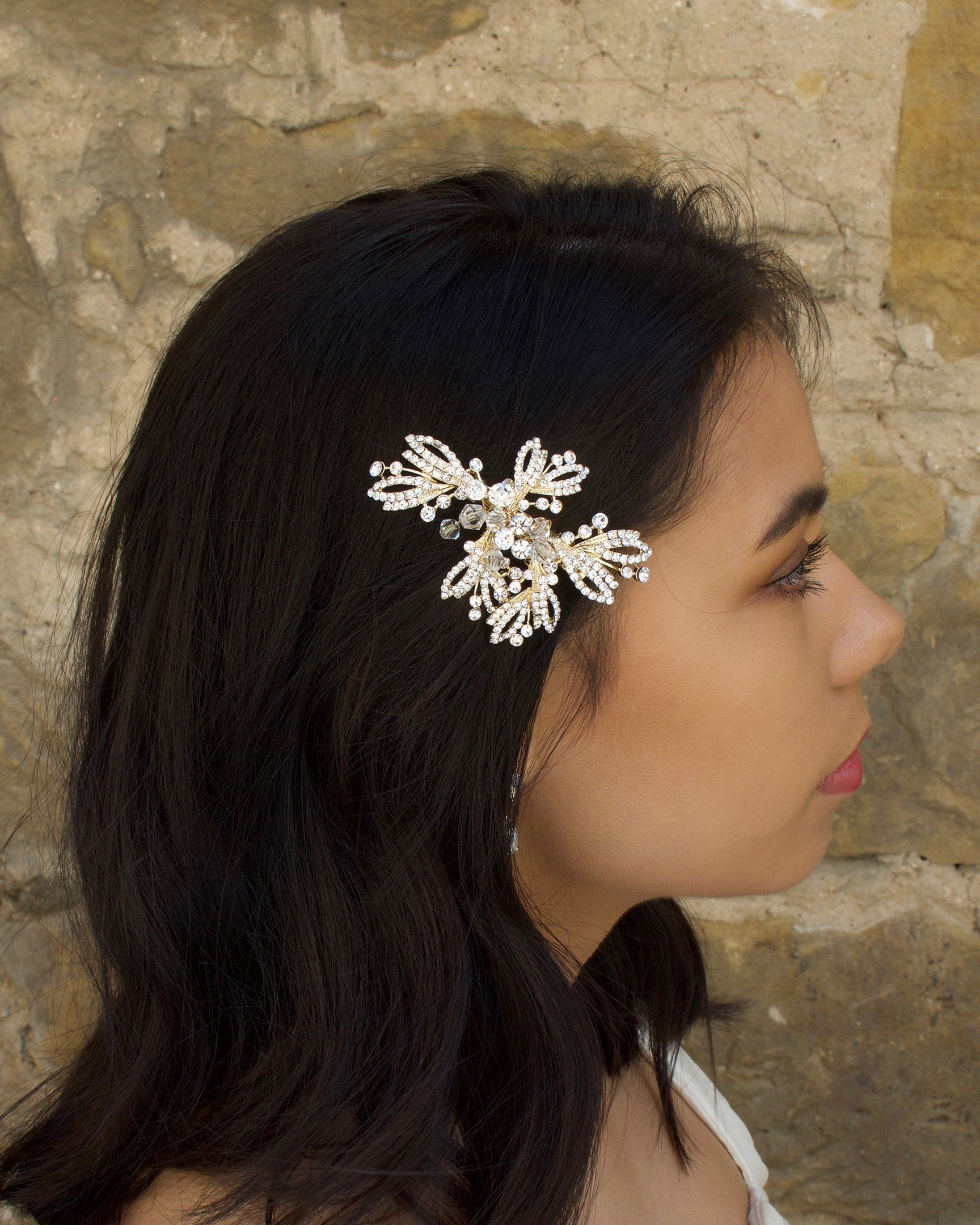 Model with dark hair wears a silver and flower side comb with a stone wall backdrop