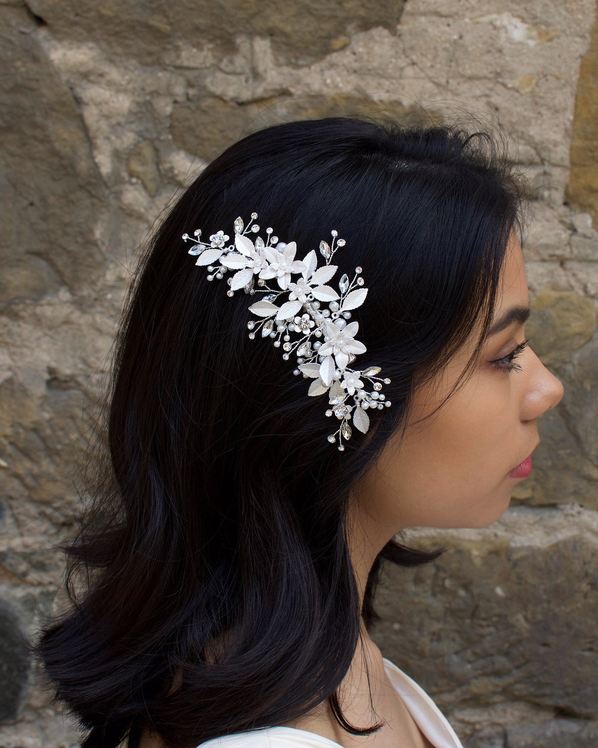Dark haired model with long hair wears a side comb of silver leaves at the side of her head.