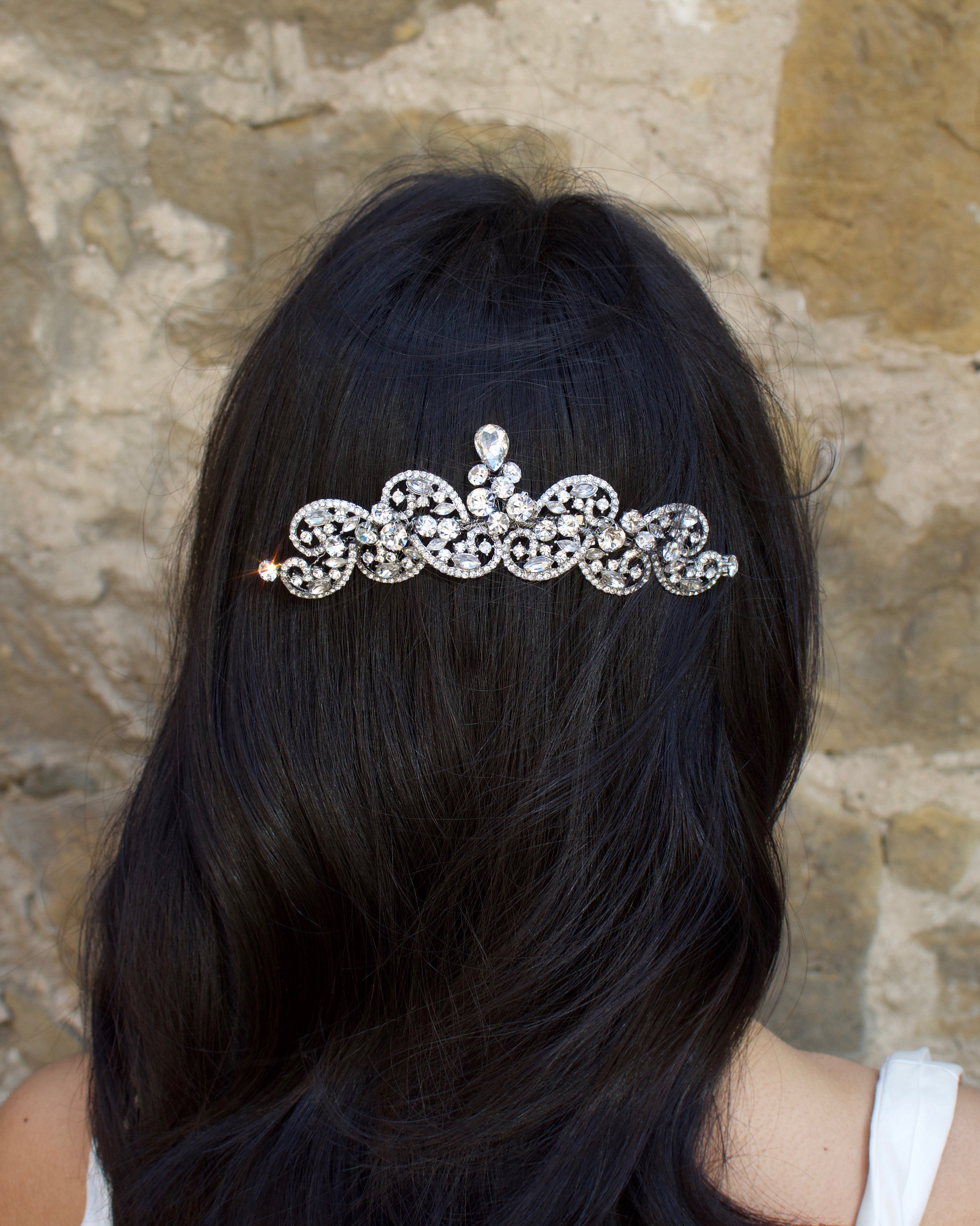 Model with long black hair wears a silver crystal comb at the back of her head in front of an old stone wall