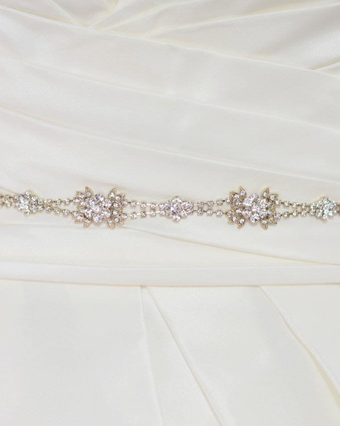The waist of a bridal dress shown with a narrow Rose Gold belt worn around it with a white background
