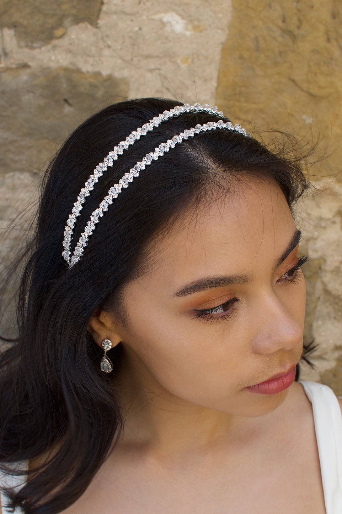 Black hair bride wearing a simple two row silver headband with a stone wall background.