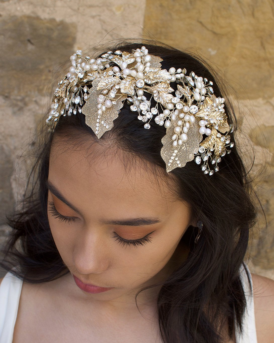 A wide gold headband worn by a dark hair bride with a stone background
