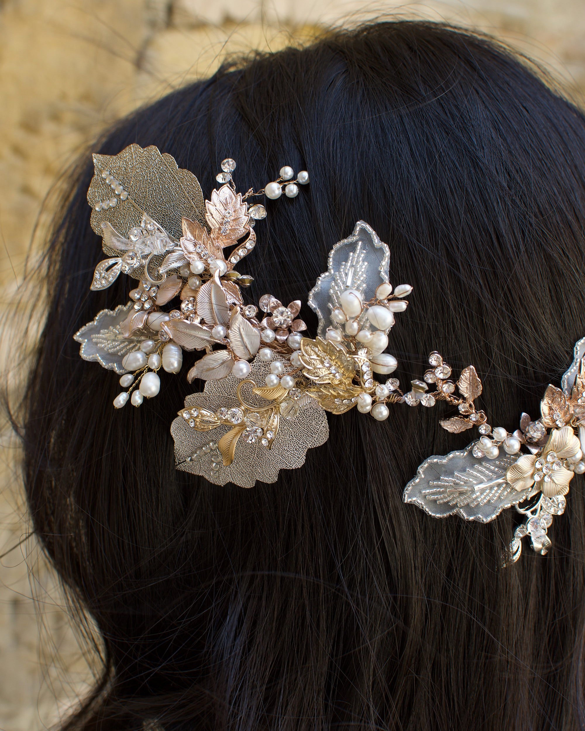 A dark haired model with hair down wears a Bridal Vine in Silver, Gold and Rose Gold with a background of a stones