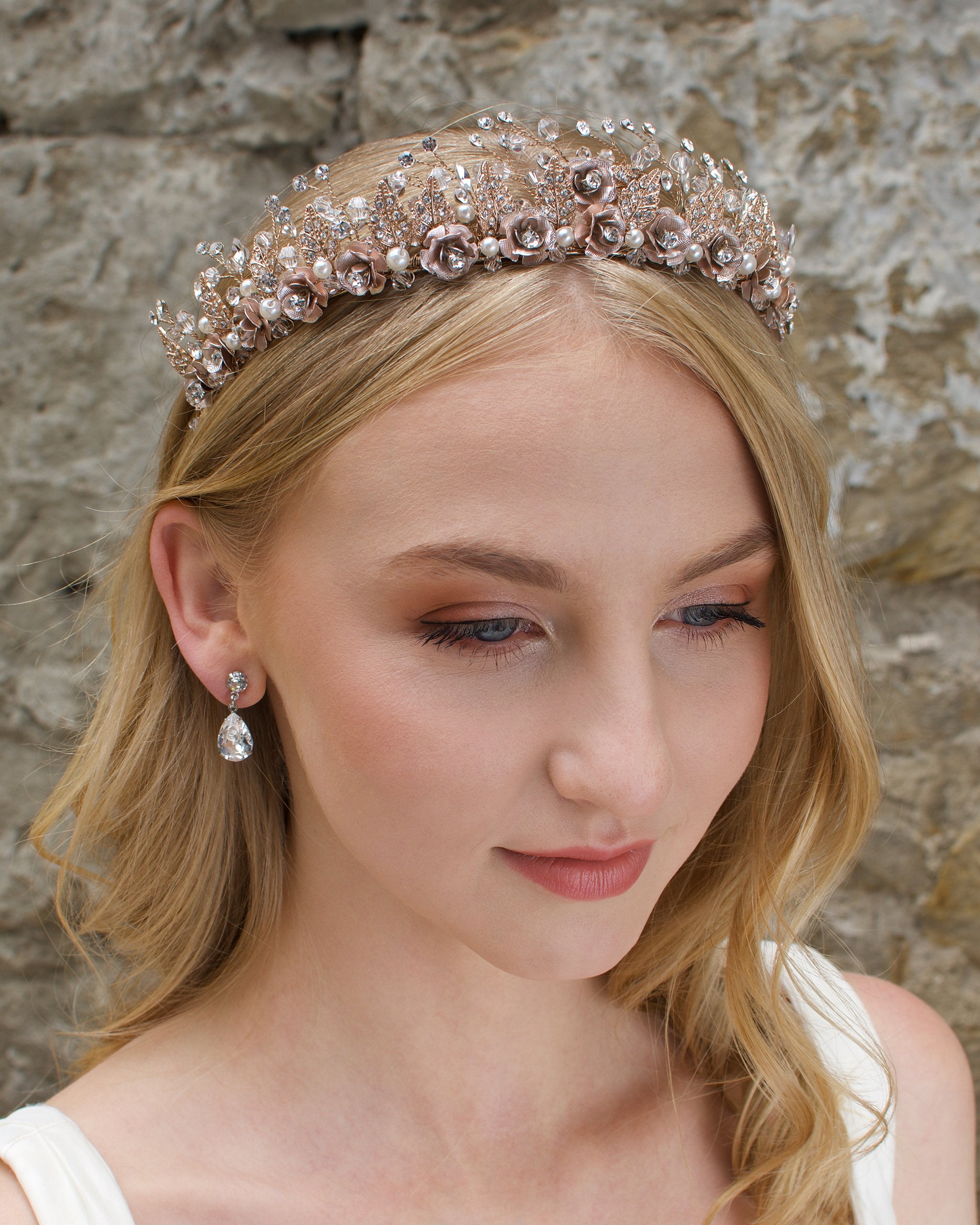 A Rose Gold Flowers and pearls wide tiara worn by a blonde bride with a stone wall background.