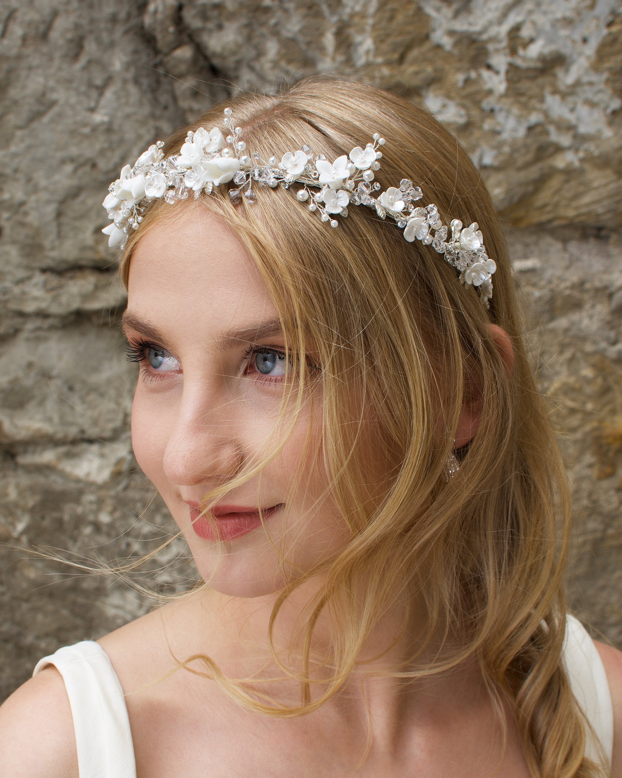 Smiling Blonde Bride wears a headband of ceramic flowers with a stone wall background