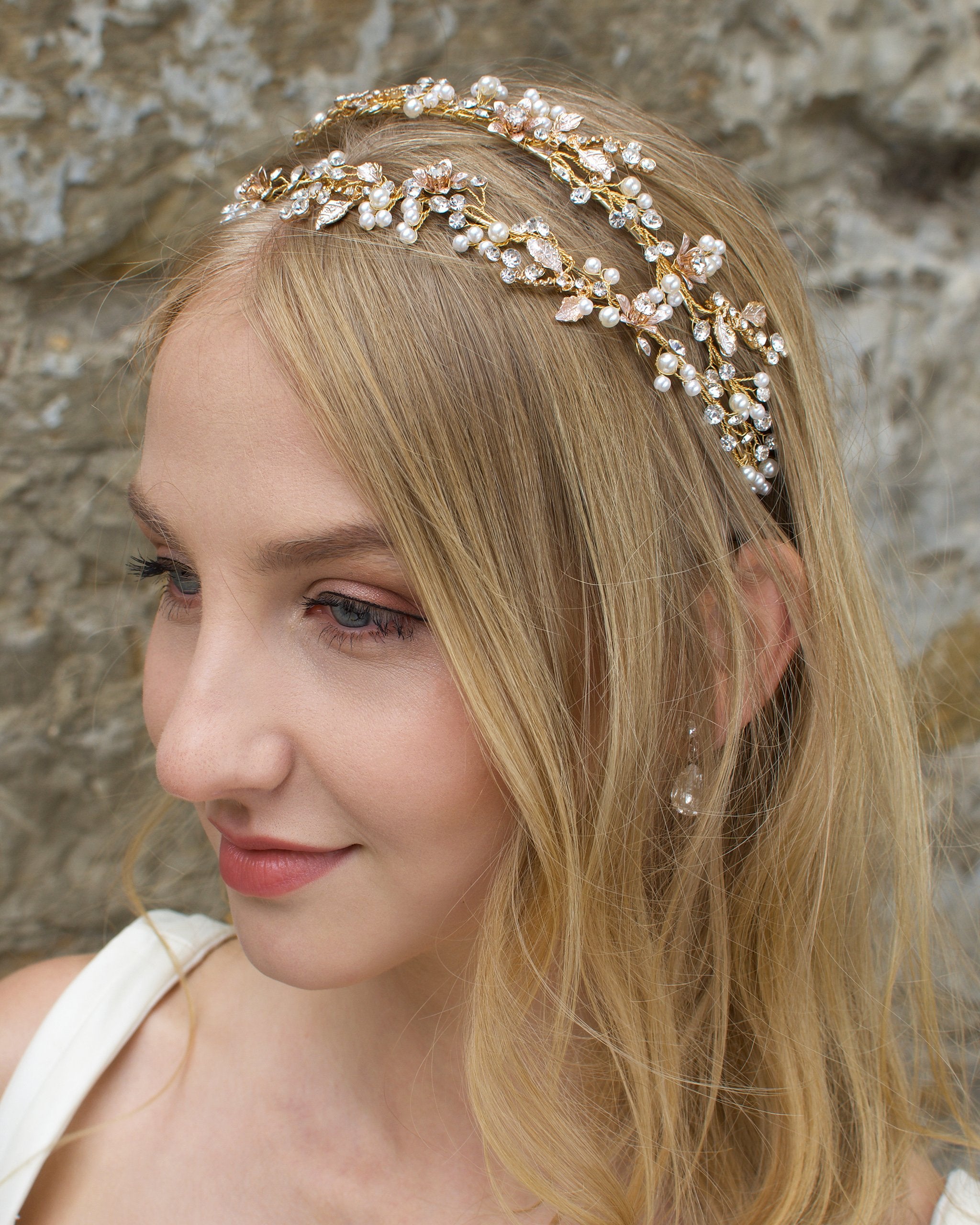 Blonde smiling bride wearing a gold and pearl headband with a stone wall backgtound