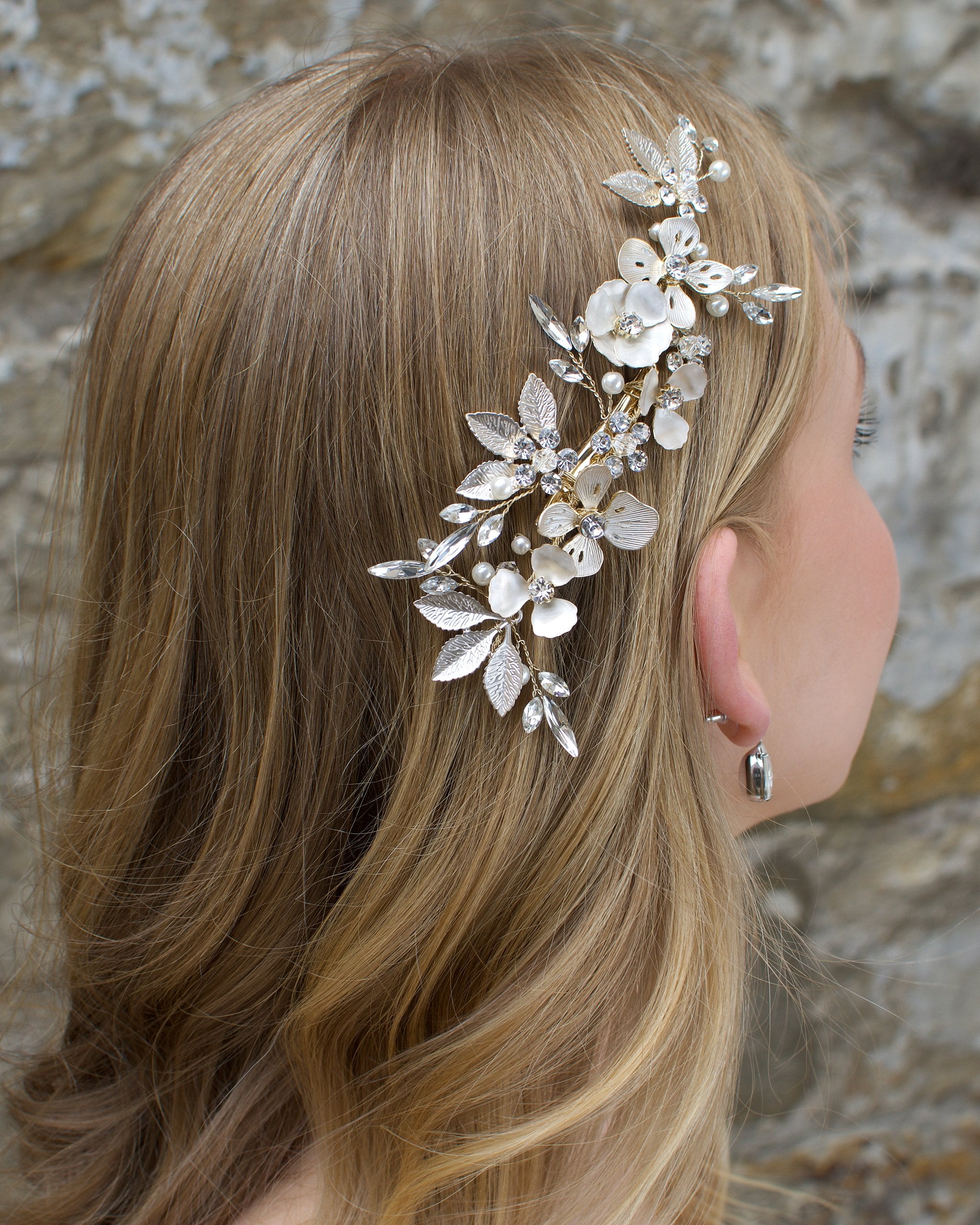 A Comb with different flowers and leaves in Pale Gold with pearls sits on the head of a blonde model bride