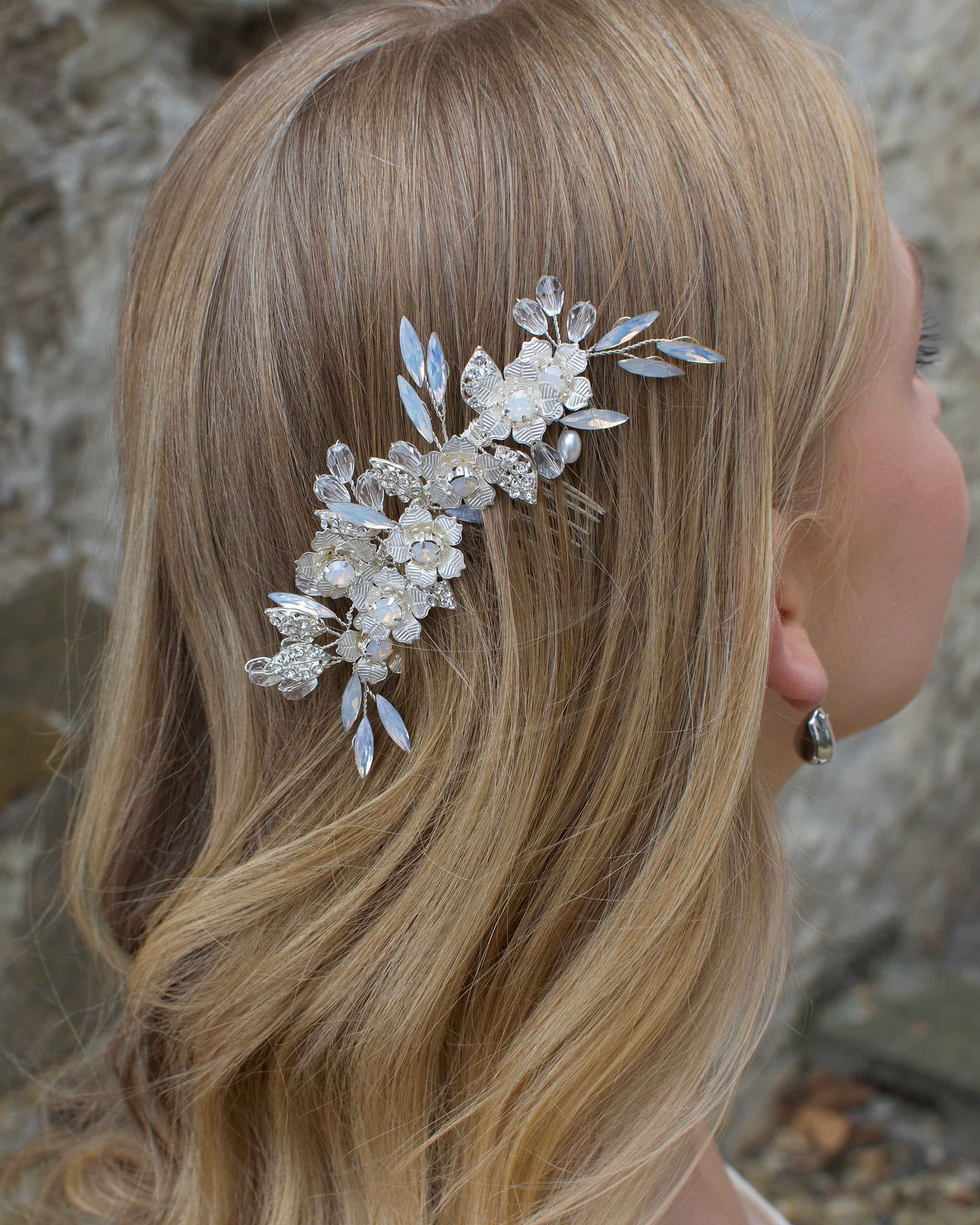 Long Blonde hair Model Bride wears a small white opal comb on the side of her head. There is a stone wall background