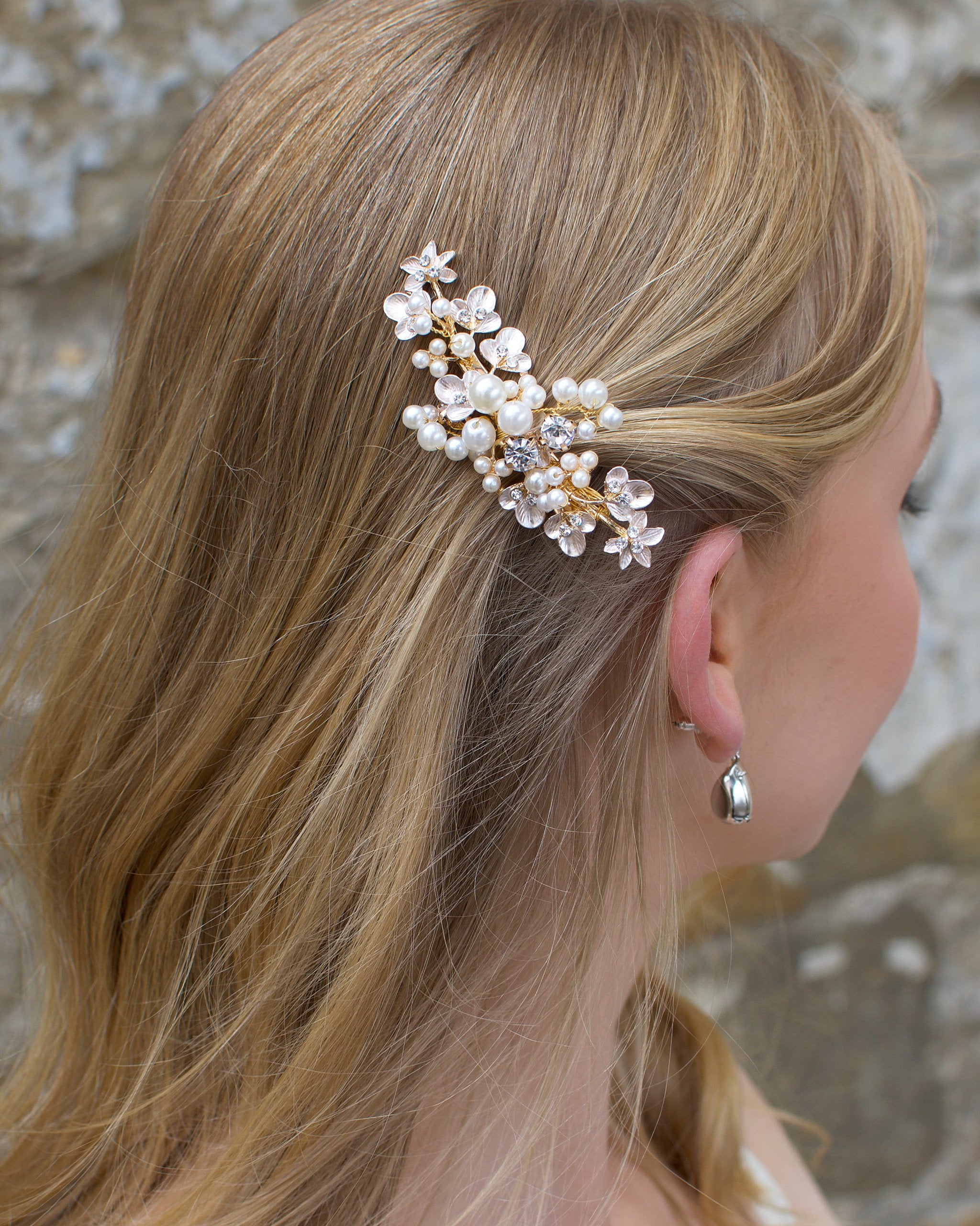 Blonde hair model wears a pearl hair clip in gold in front of an old stone wall