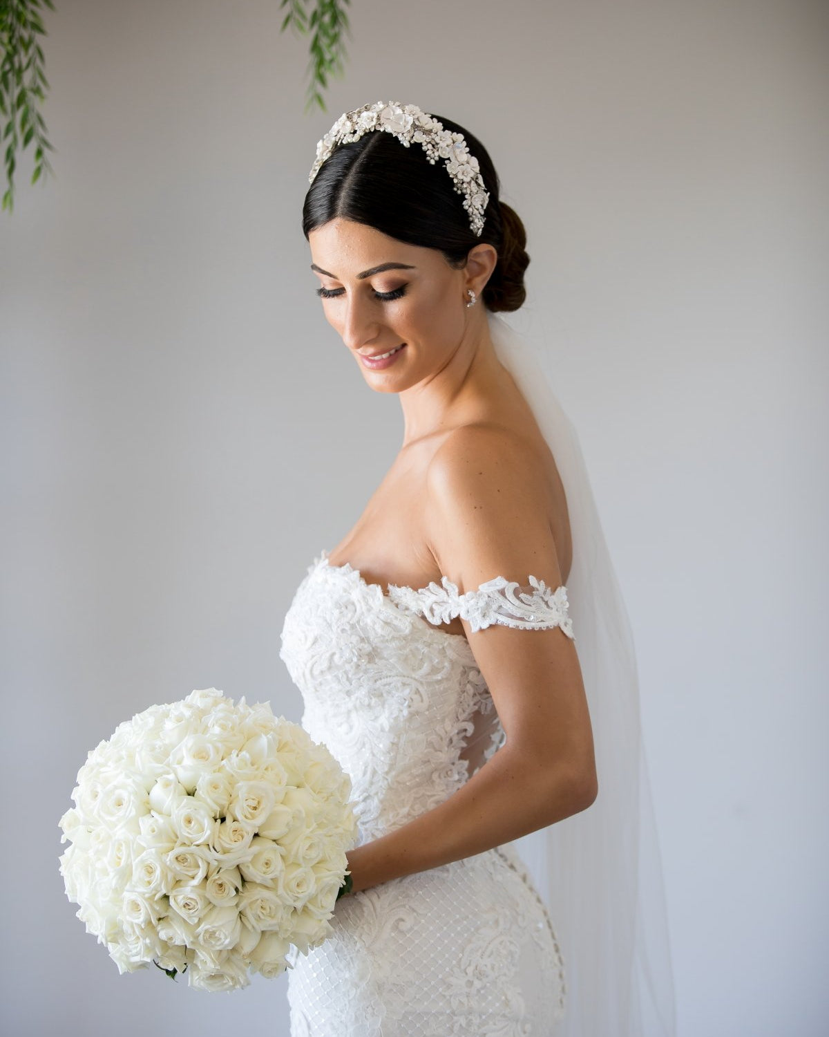 A bride wears a headband of ceramic flowers on her dark hair. There are green leaves in the background