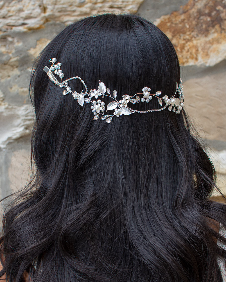 A woman with dark hair wearing a silver and pearl bridal hair vine adorned with sparkling leaves and pearl beading.