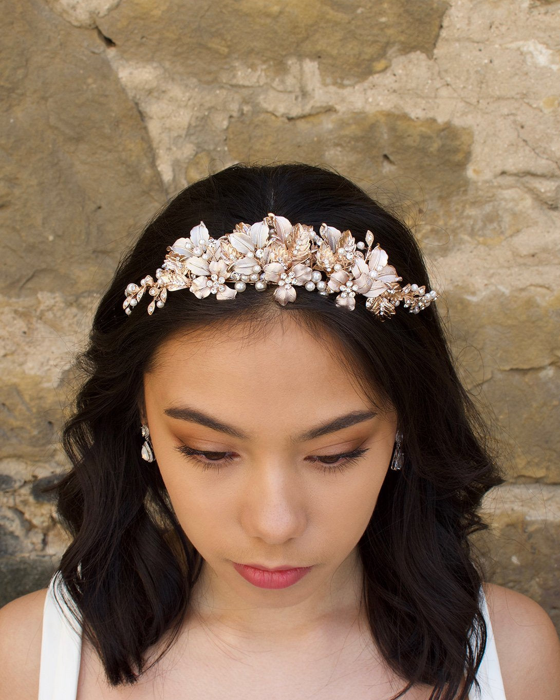 Black haired model wears a pale rose gold and pearl low bridal headband with a stone wall behind