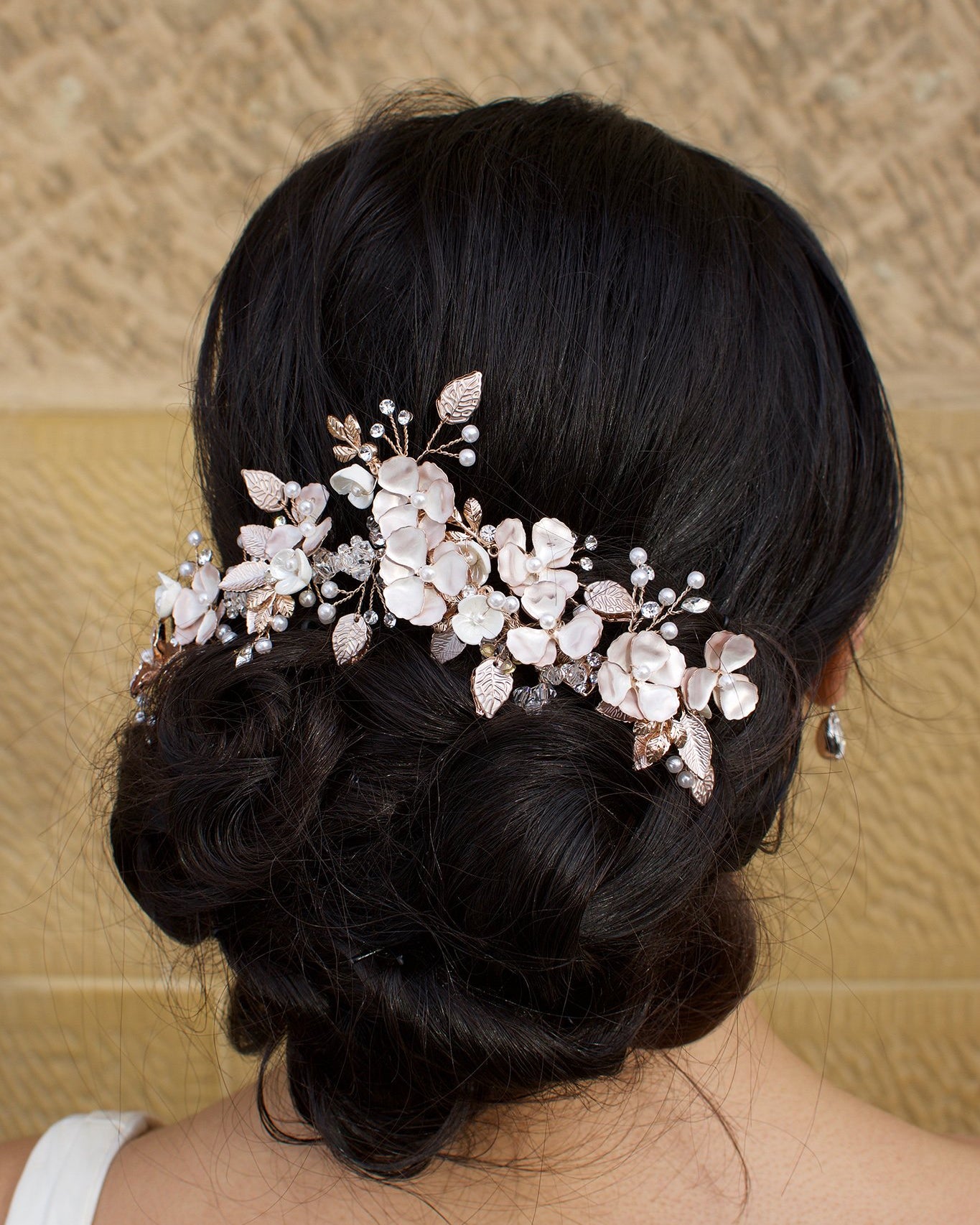 Bride wears a Pale Rose Gold Bridal headpiece in her dark curly hair with a stone wall background
