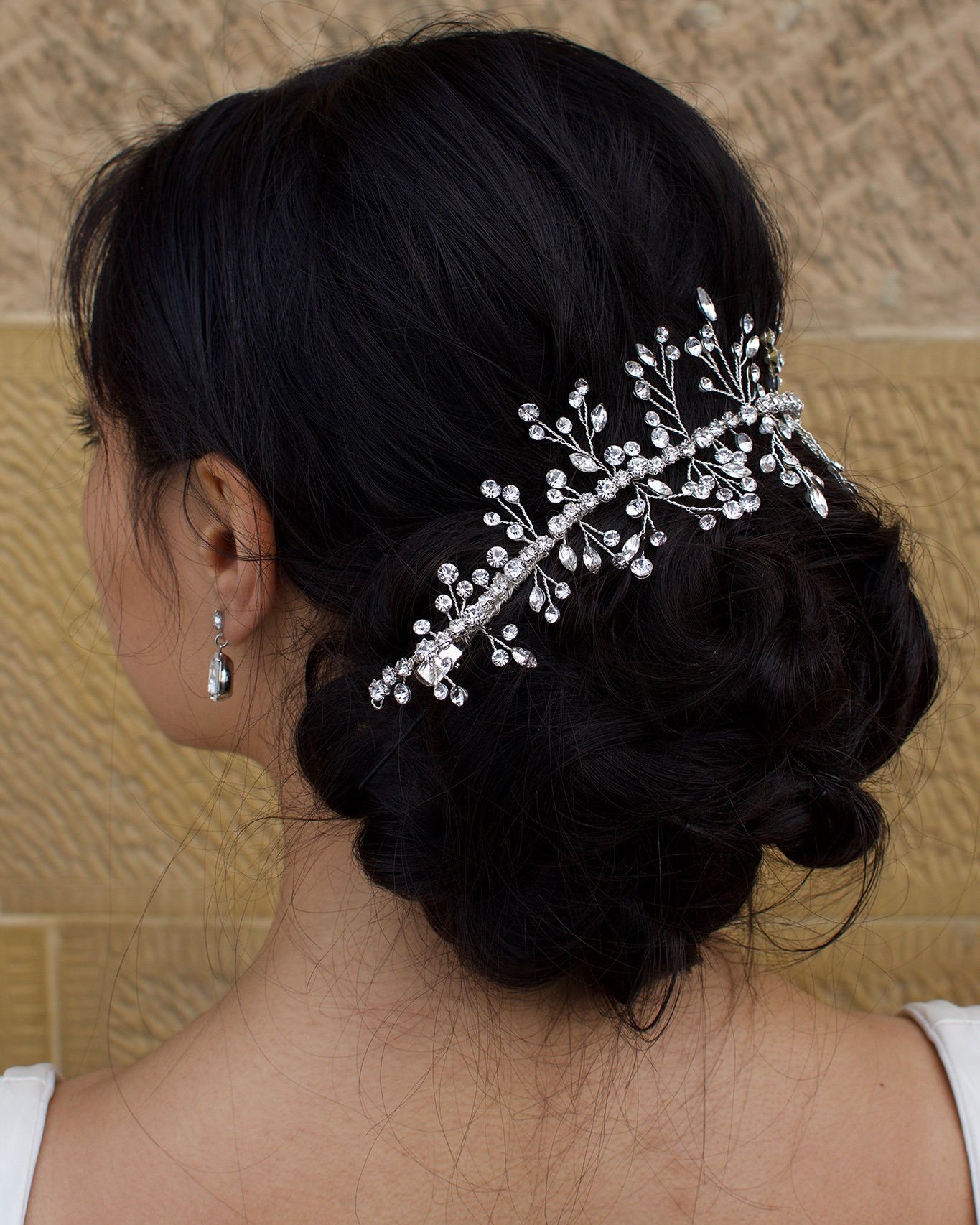 Black Hair Bride wearing a Silver Crystal vine around the back of her hairstyle with a stone wall background