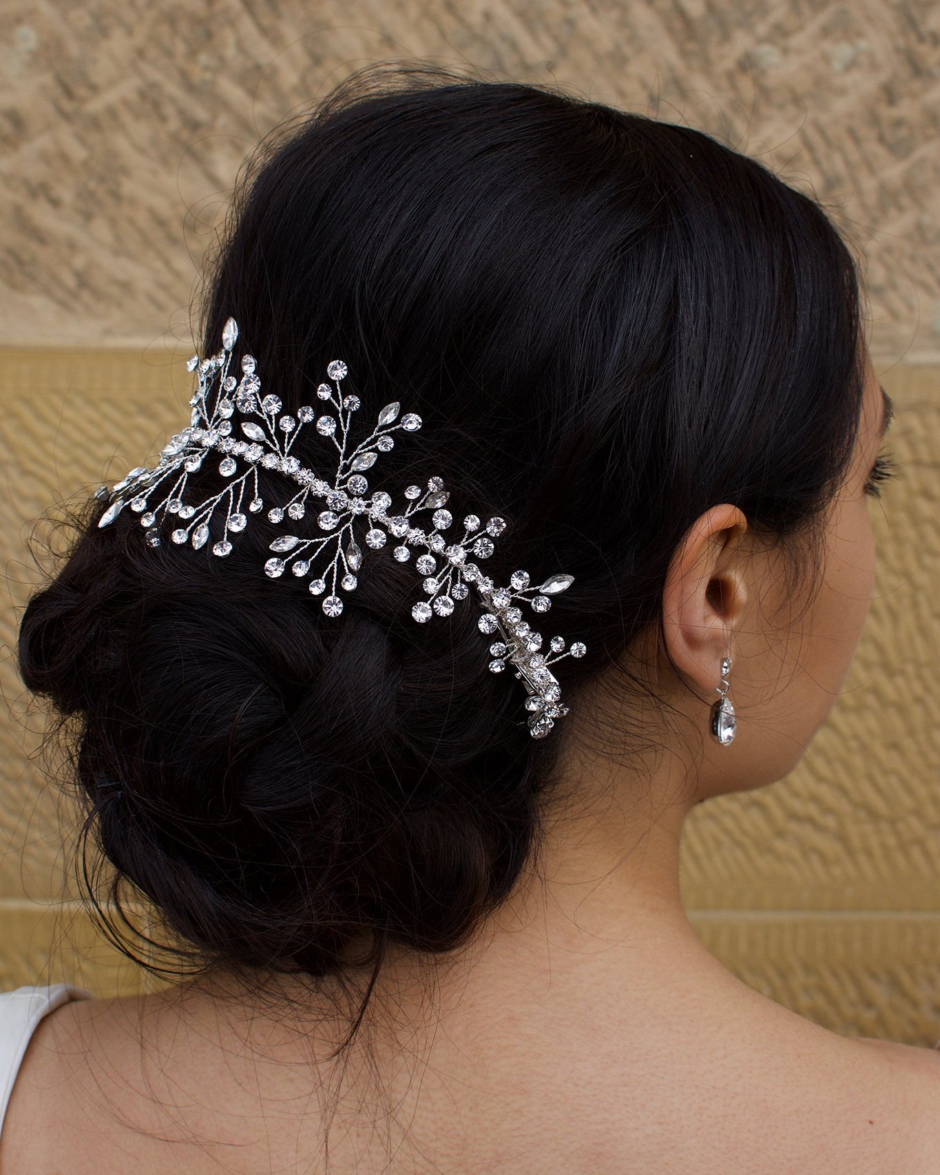 Dark hair model wearing a silver bridal vine around the back of her hair with a sandstone wall backdrop