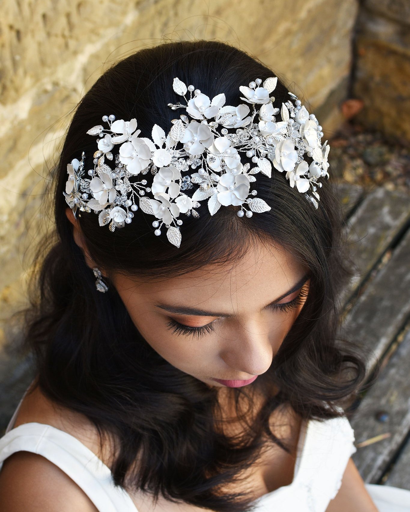 Black Haired model wears a wide headband of flowers with the background of a stone wall