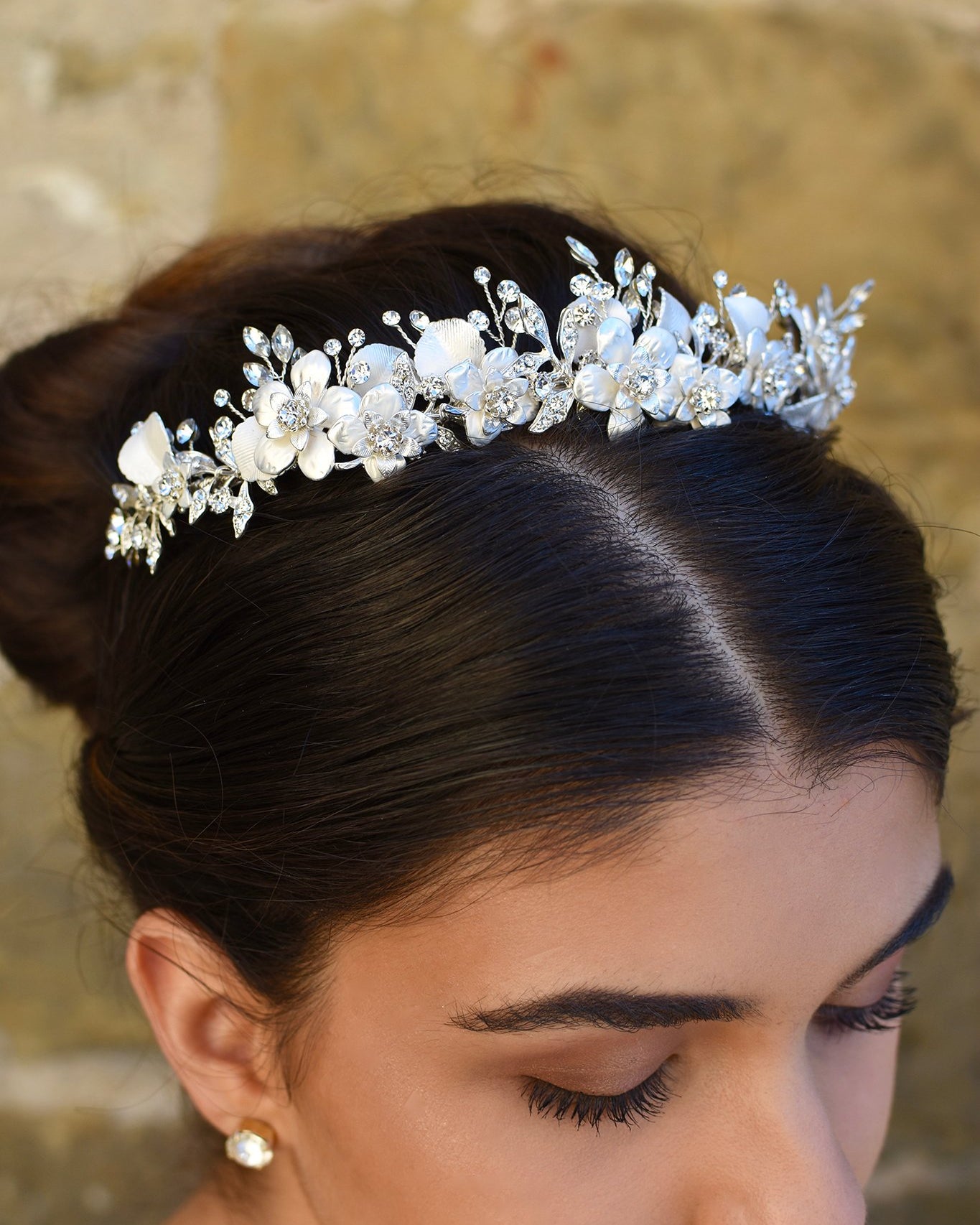 Close up of a white and silver bridal tiara with flowers and leaves worn by a dark hair model with her hair up