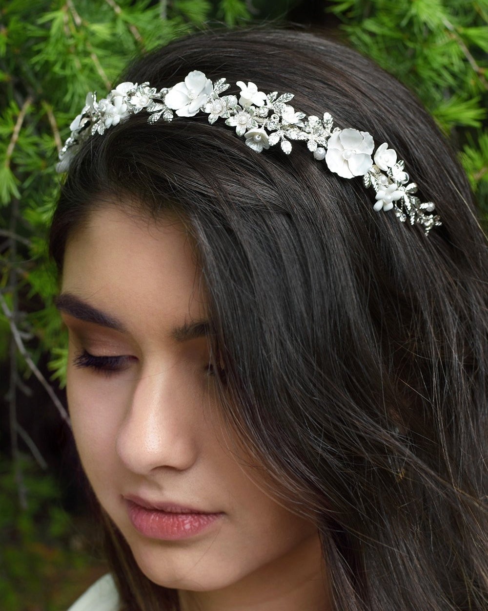 Dark hair model wearing a silver and flowers bridal headband with a pine tree bsckground