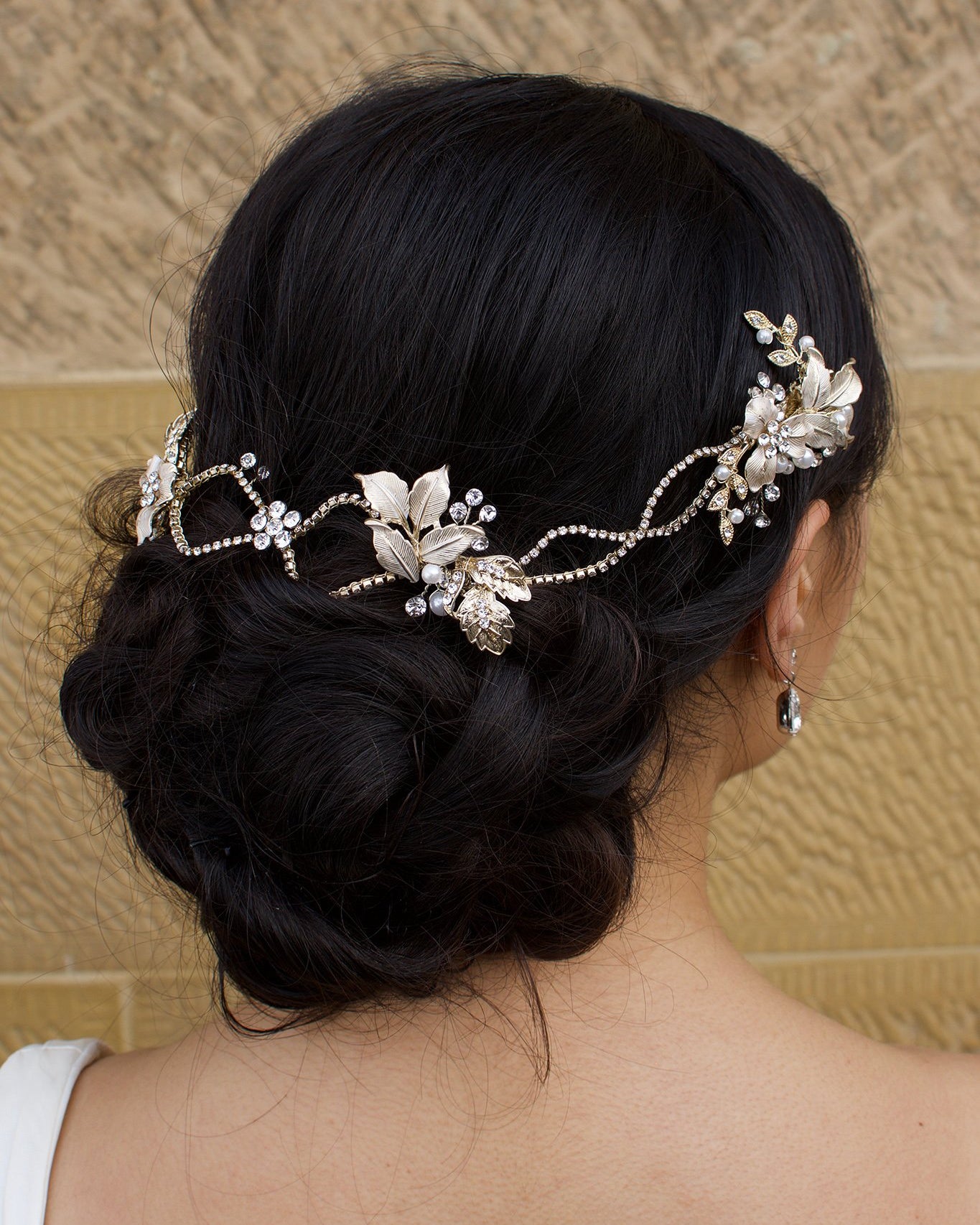 A dark haired model with curly hair wears a pale gold bridal vine at the back of her head